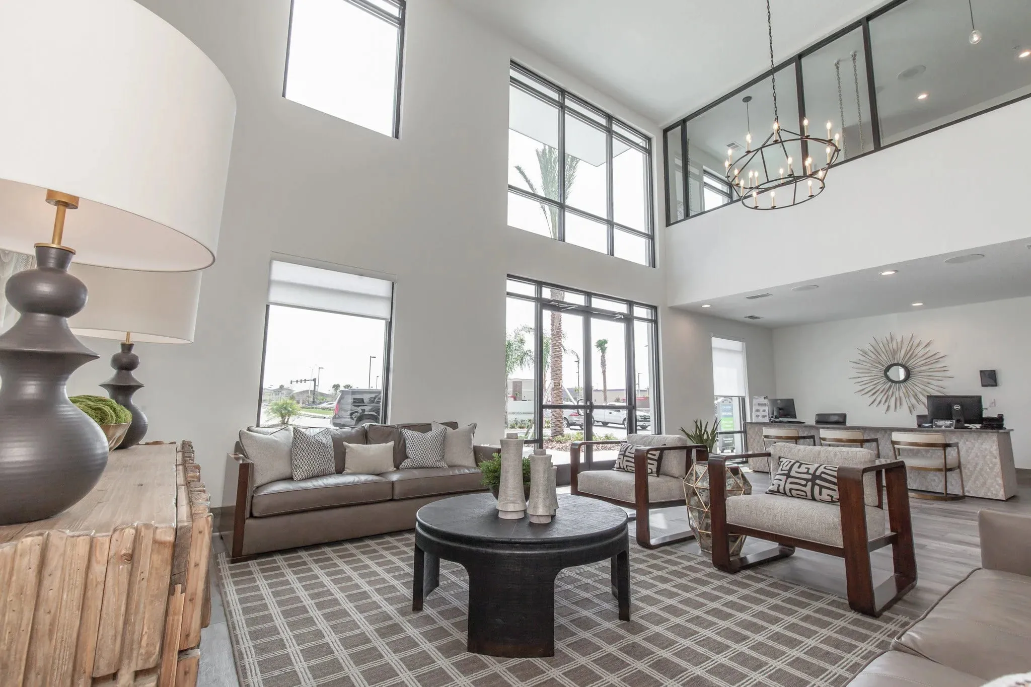 Multifamily amenity leasing lounge with an iron ring chandelier above sofas and wood-framed chairs beside the leasing desks