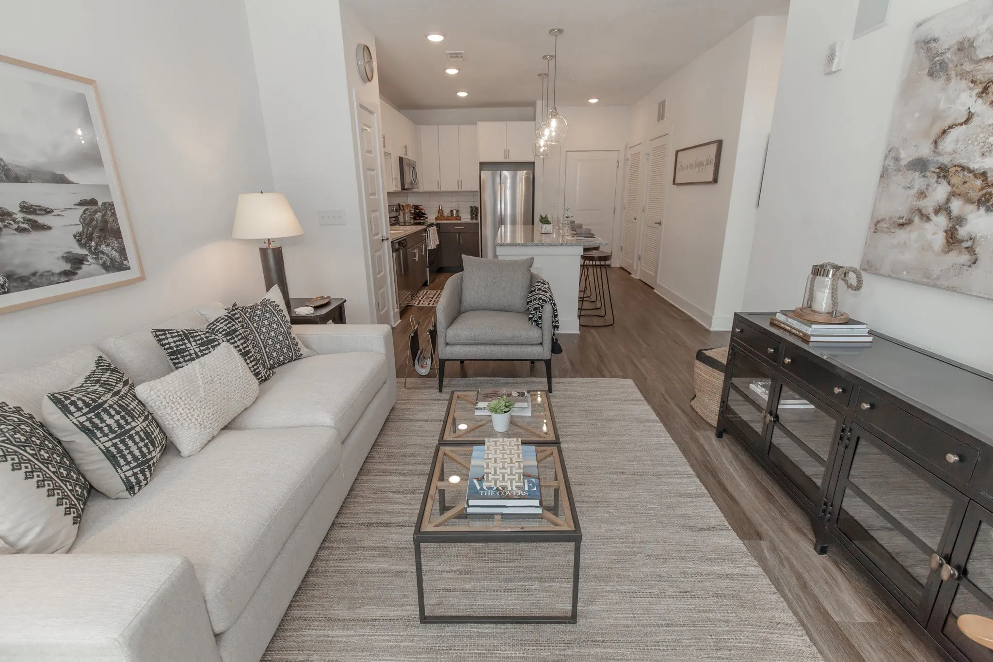 Multifamily apartment model living room with a white sofa and glass coffee table open to the kitchen beyond