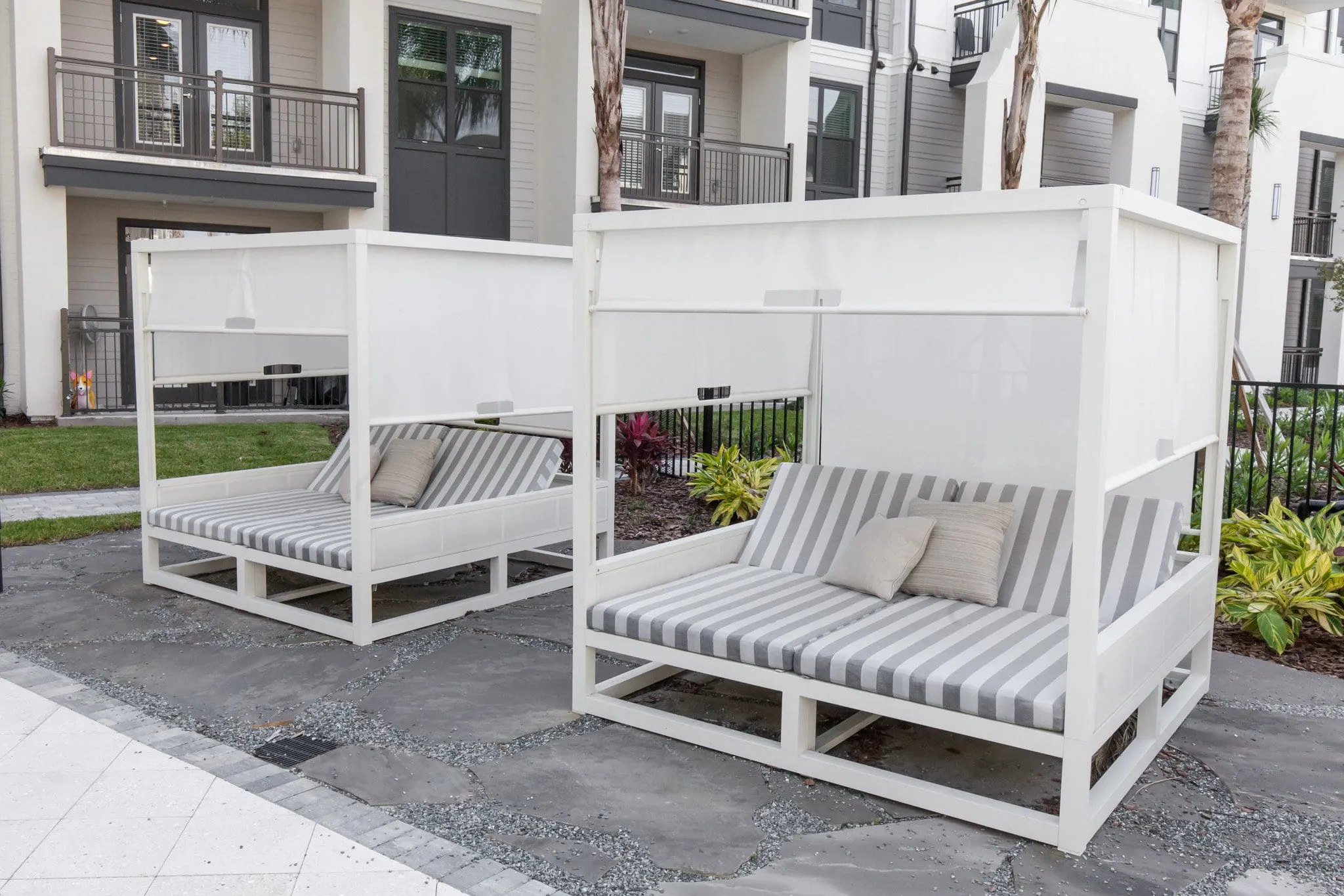 Multifamily community cabanas, white canopy daybeds with striped cushions beside the residences