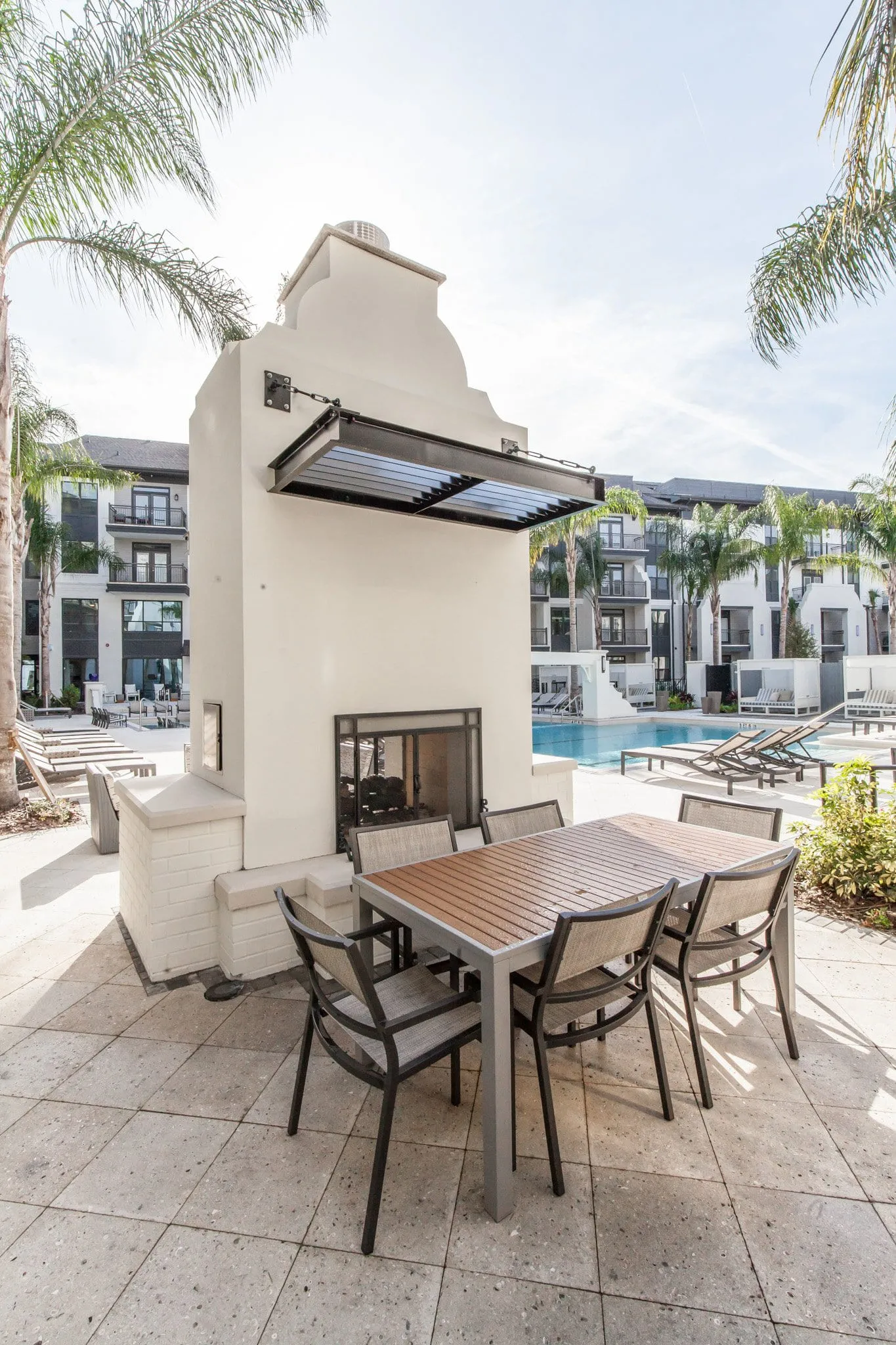 Multifamily community terrace with a stucco fireplace and dining table looking out to the pool and palms