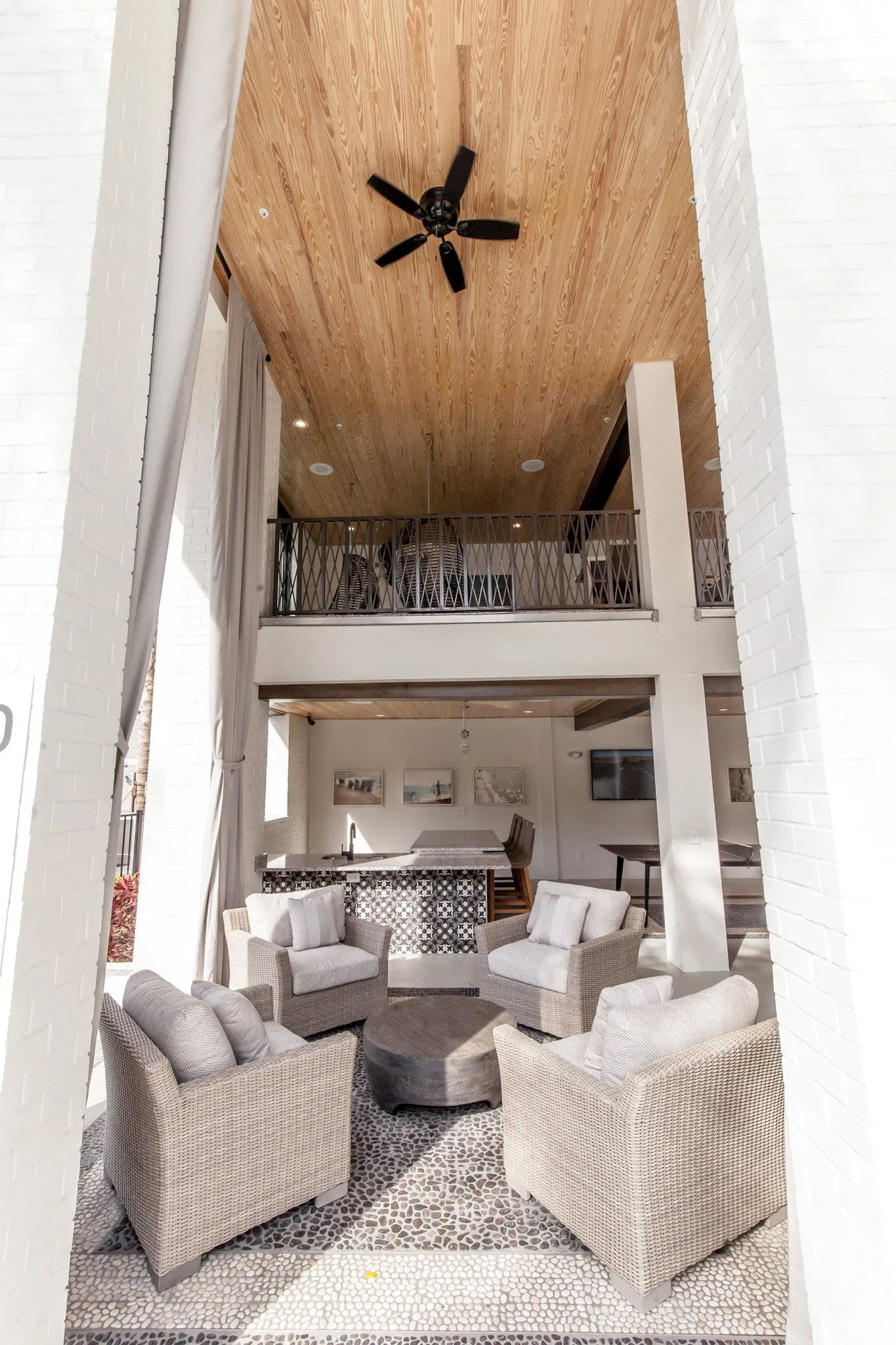 Multifamily amenity two-story lobby with a wood-clad ceiling and iron balcony rail above white lounge seating