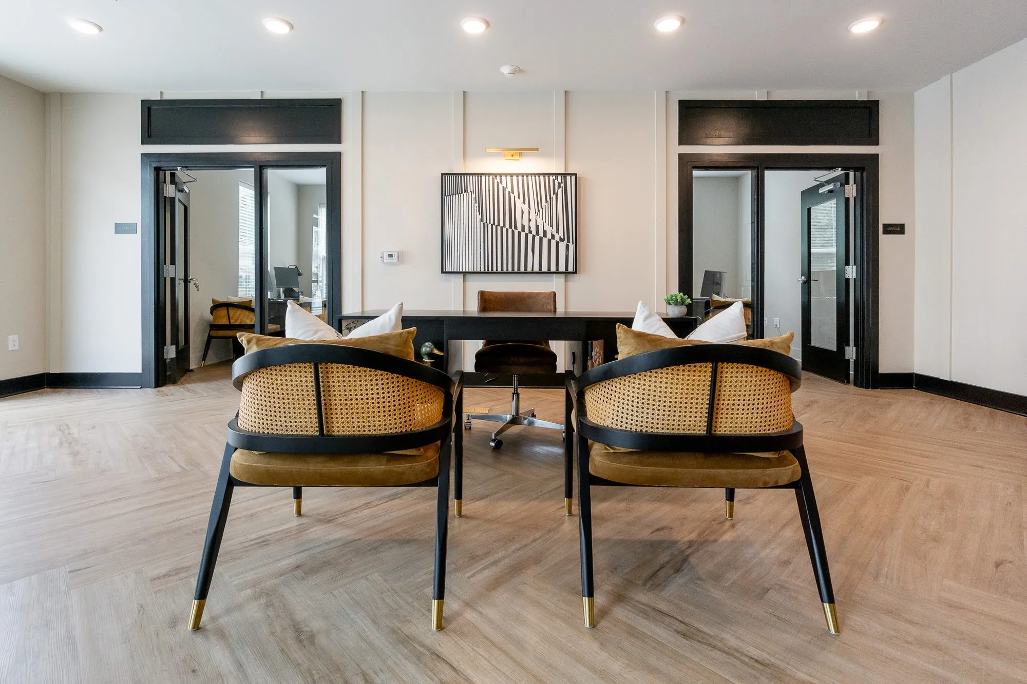 Multifamily amenity leasing area with cane-back chairs facing a black desk, a black and white abstract between glazed doors