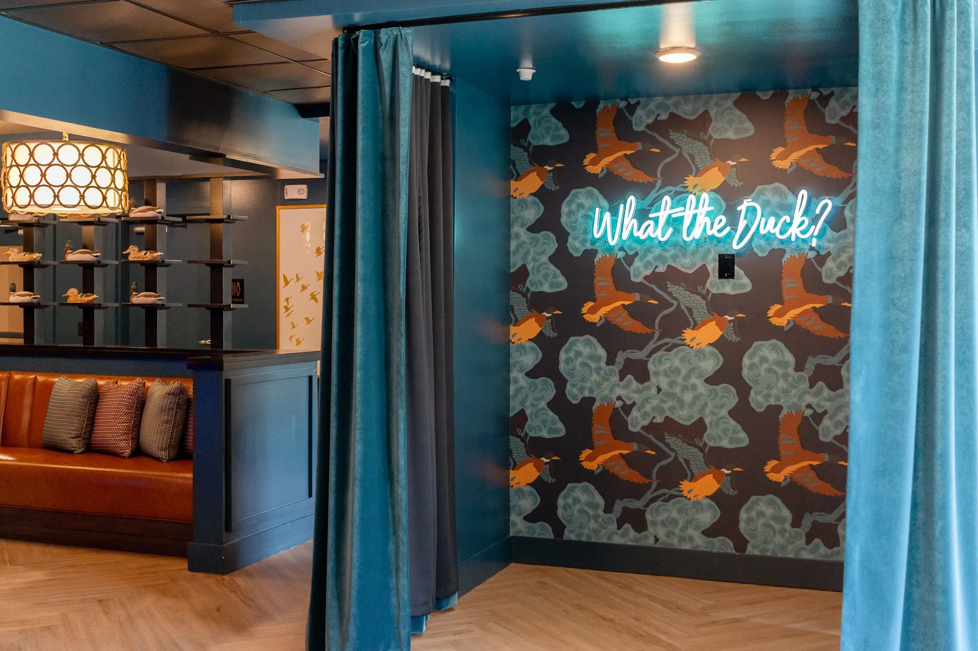 Multifamily amenity neon What the Duck? alcove with duck decoy shelving and a leather banquette at left