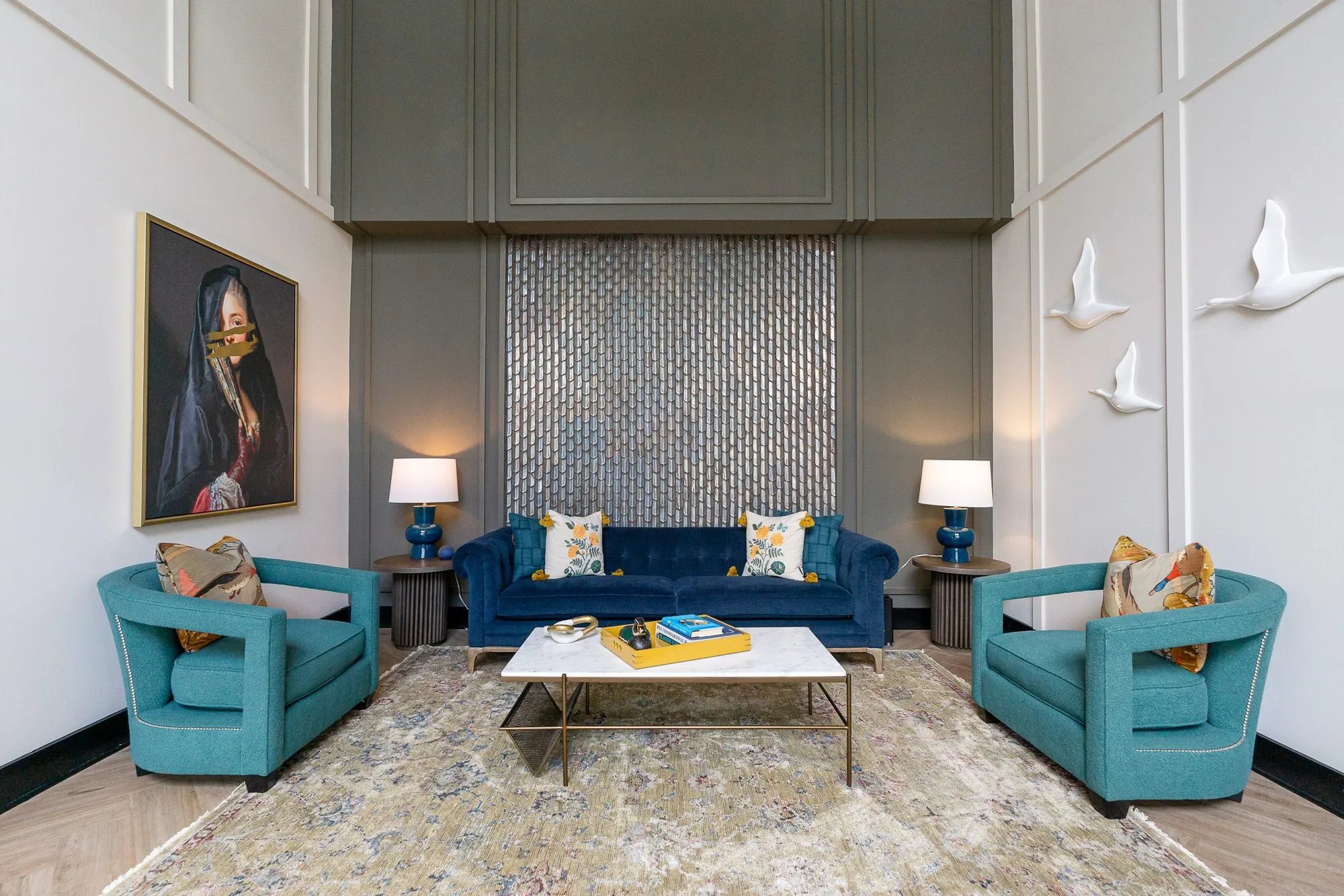 Multifamily amenity double-height lobby lounge with a navy tufted sofa between teal armchairs and a veiled portrait