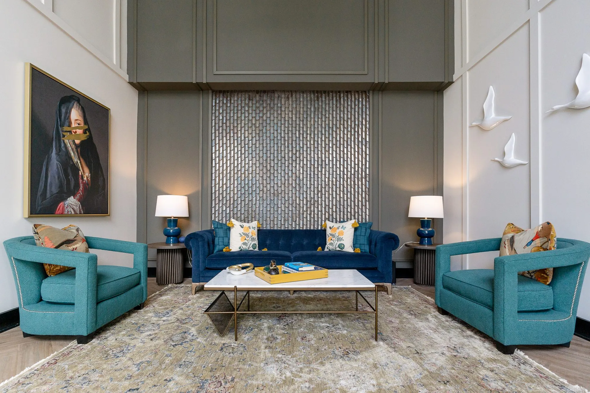 Multifamily amenity lobby lounge with the navy tufted sofa and teal armchairs below a shimmering tile panel