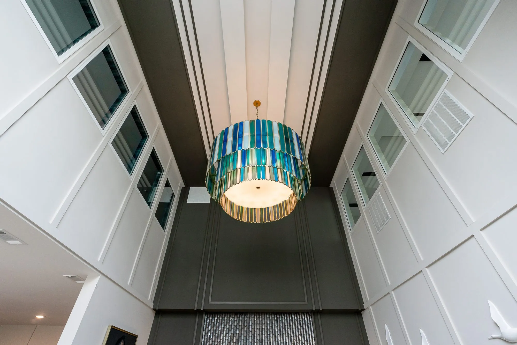 Multifamily amenity lobby looking up at a tiered blue and green glass chandelier and clerestory windows