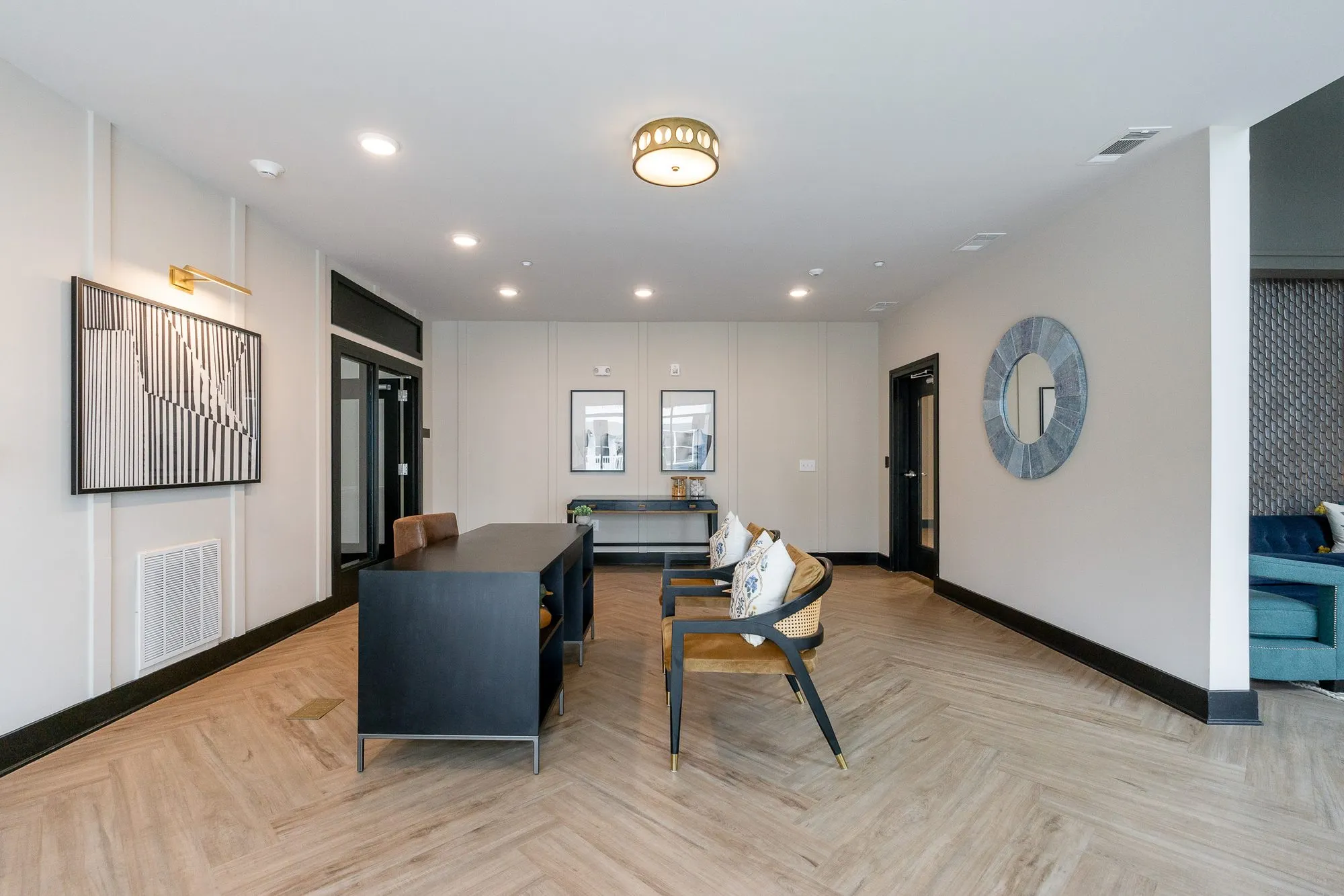 Multifamily amenity leasing area with a black desk and cane chairs on a herringbone floor, a black and white abstract