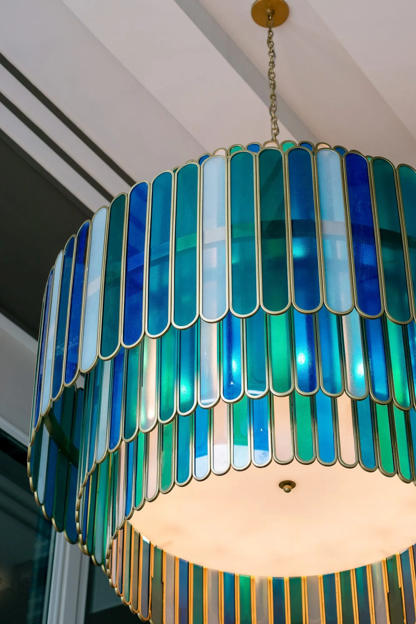 Multifamily amenity lobby chandelier seen from below, tiers of blue, green and clear glass fins with brass edges