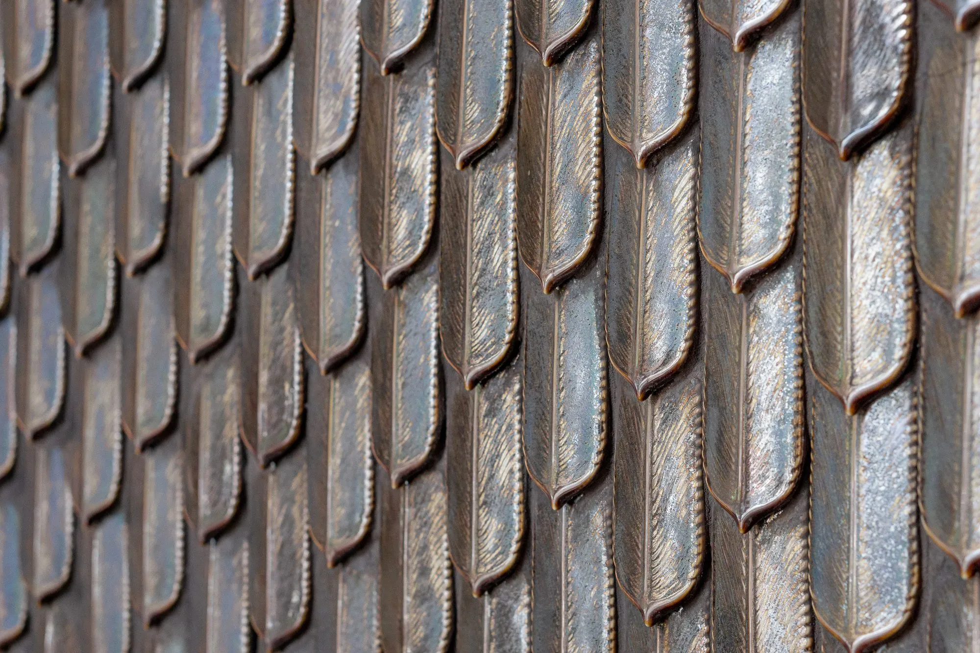 Multifamily amenity lobby wall of overlapping feather-shaped tiles in bronze and silver