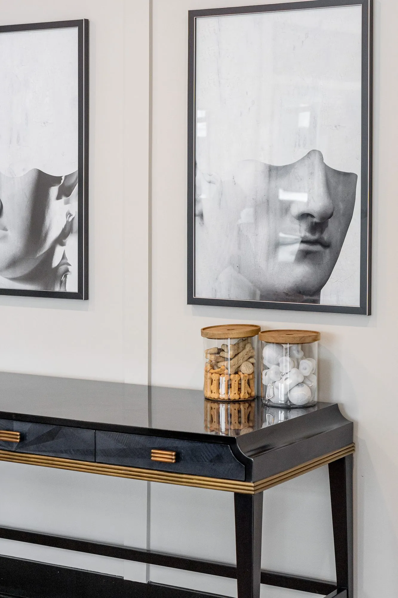 Multifamily interior detail: two black and white prints of classical faces above a black lacquer console with glass canisters