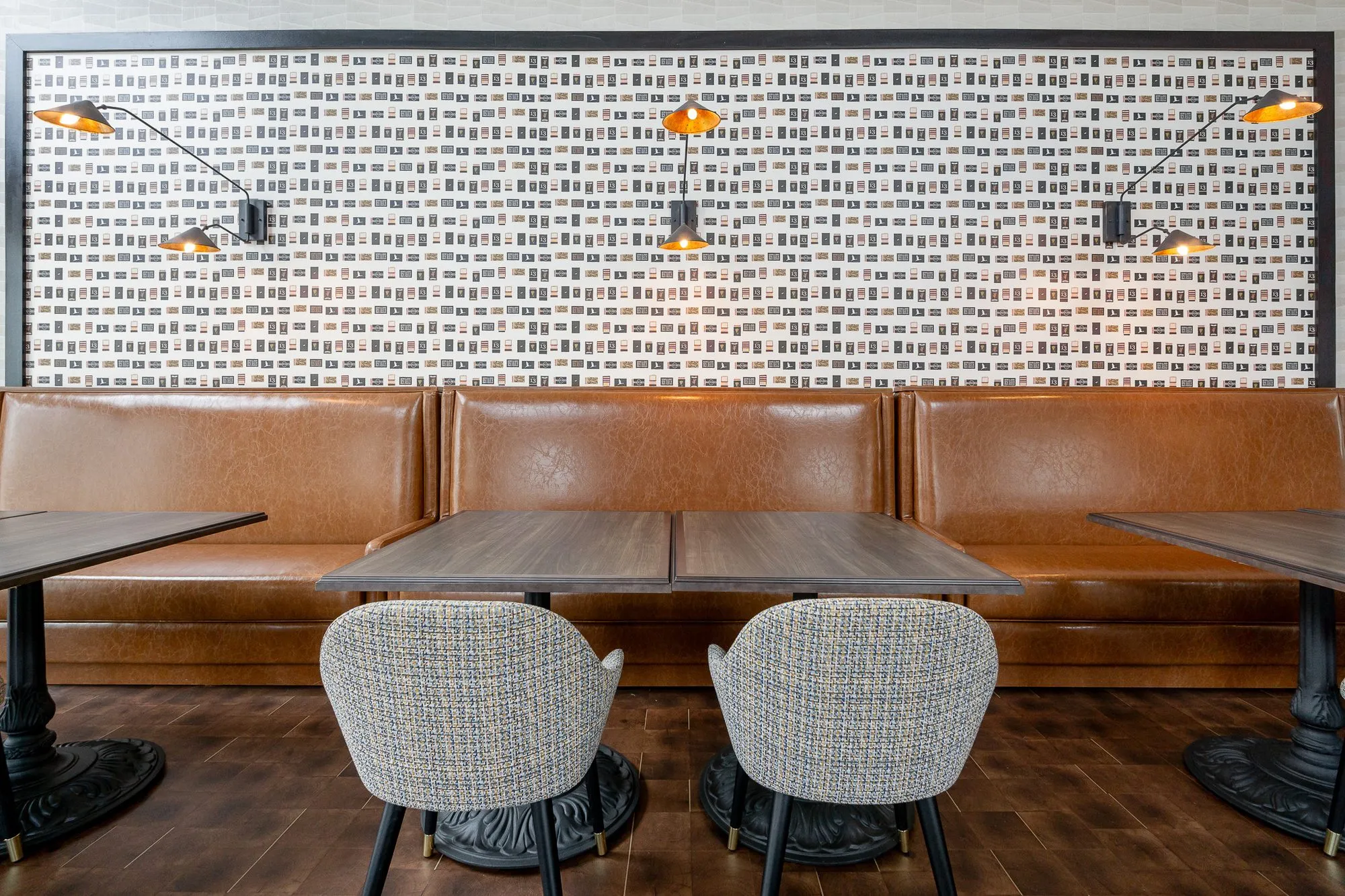 Multifamily amenity clubroom with tan leather booths and grey woven chairs below matchbook-print wallpaper and sconces