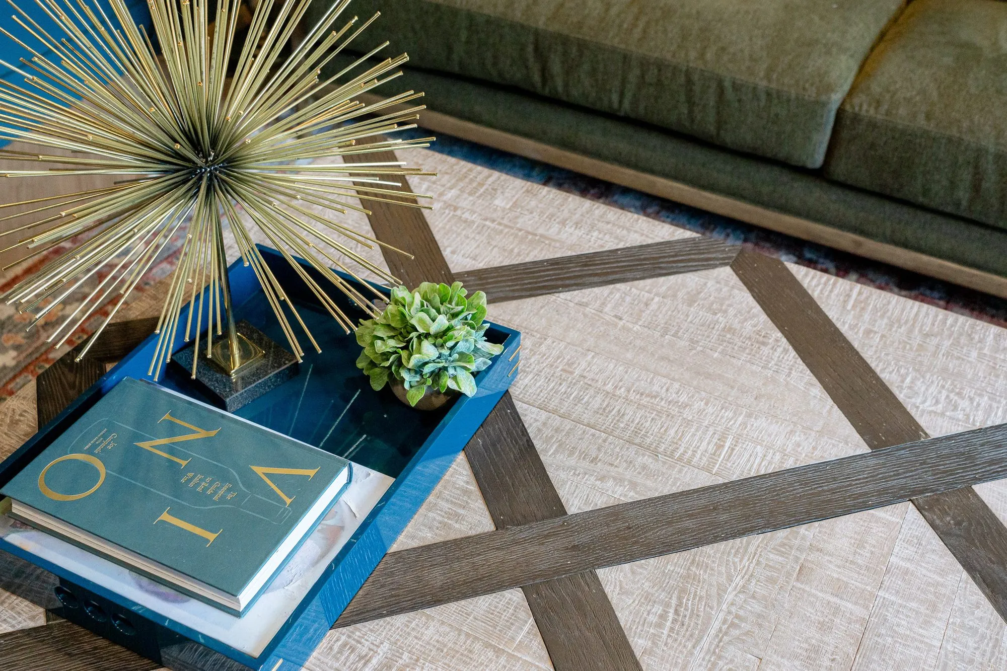 Multifamily interior detail: blue tray with a book, gold starburst and plant on a whitewashed coffee table with dark bands