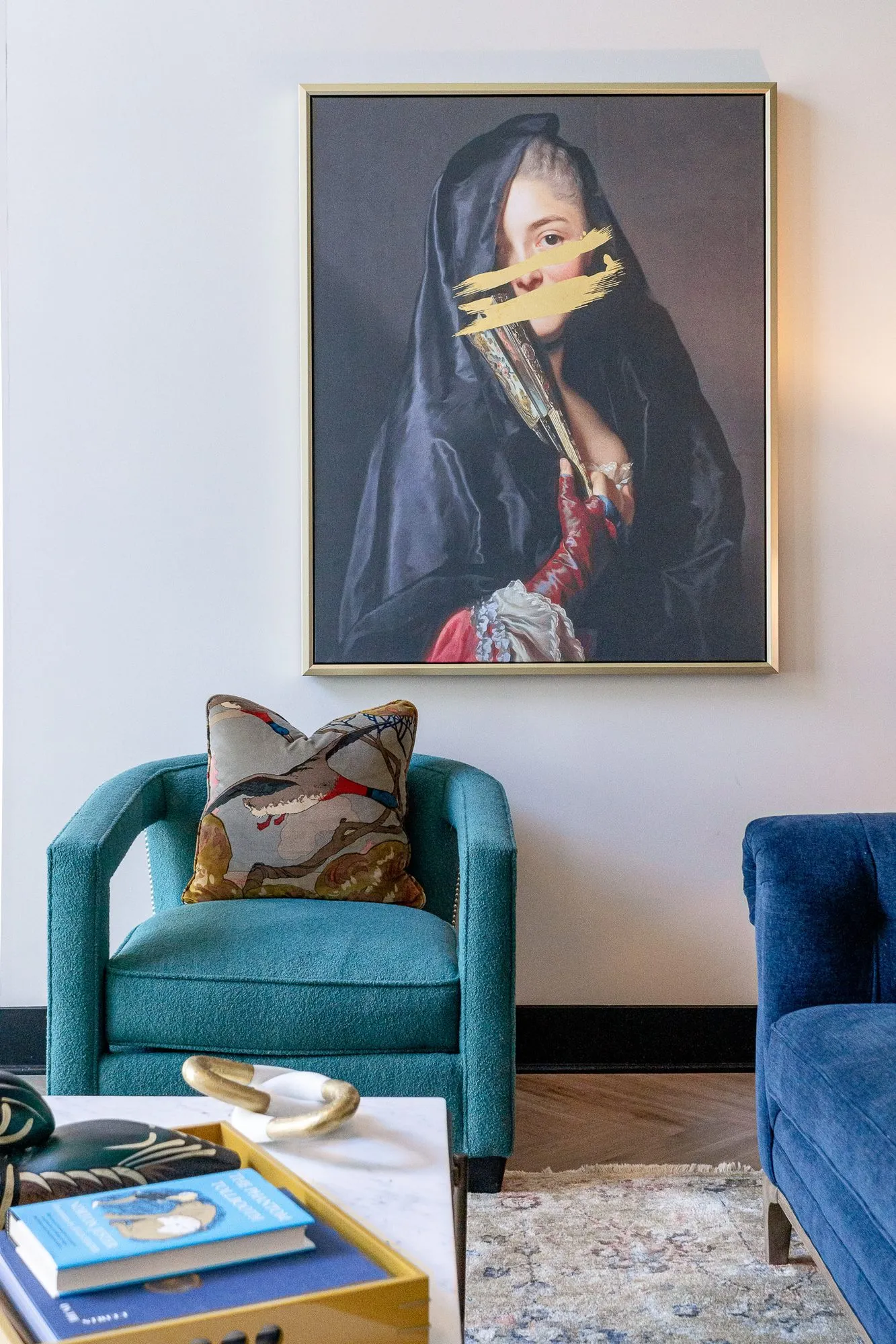 Multifamily amenity lobby lounge with a teal armchair and bird print pillow below a portrait of a veiled woman