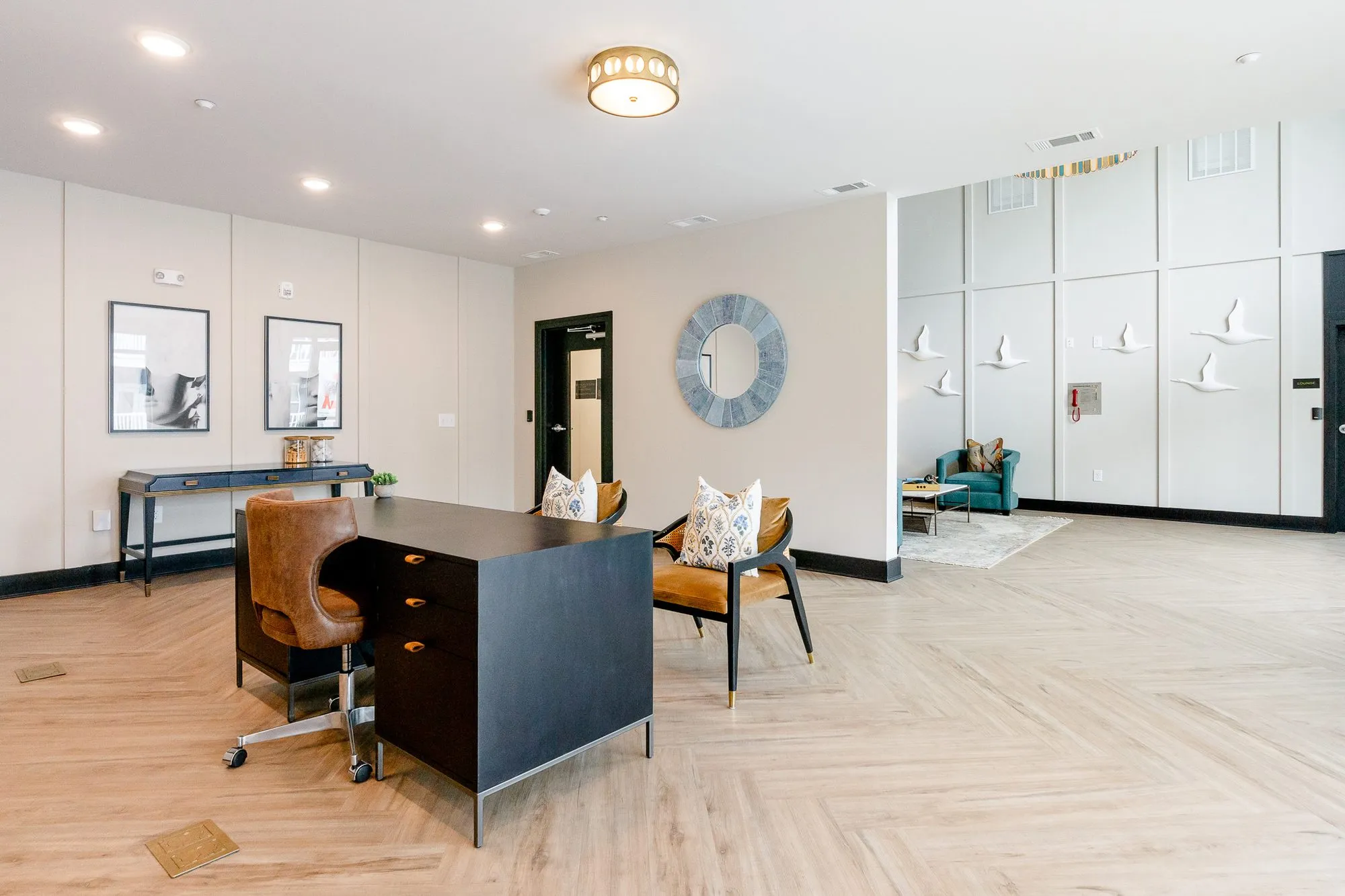 Multifamily amenity leasing desk with a cognac leather chair and two cane armchairs, white bird sculptures on the far wall