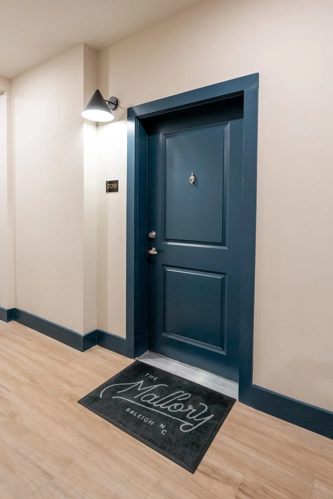 Multifamily residential corridor with a navy apartment door and a logo doormat in front