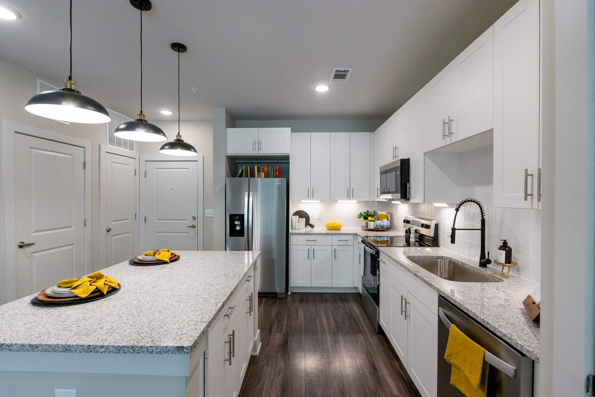 Multifamily apartment model kitchen with white cabinets, granite counters and black dome pendants over a set island