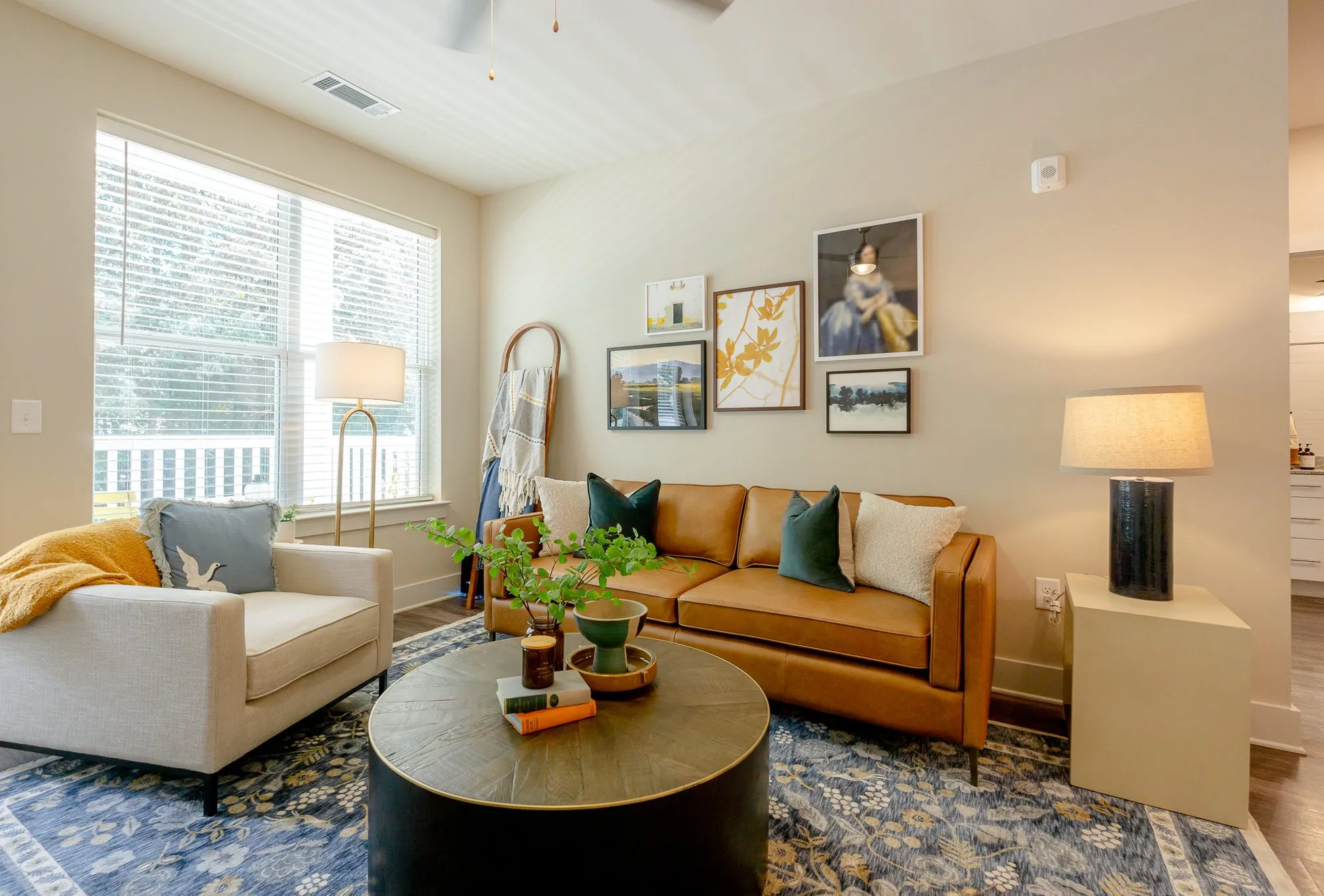 Multifamily apartment model living room with a cognac leather sofa, a cream armchair and round coffee table, gallery wall