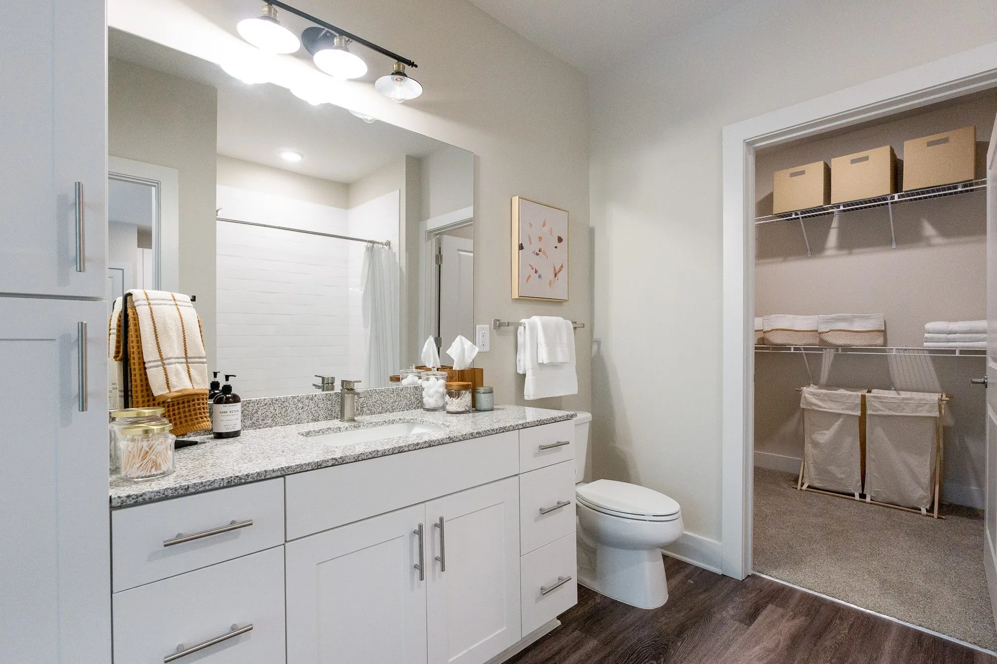 Multifamily apartment bathroom with a white vanity and granite top beside a walk-in closet of shelves and woven hampers
