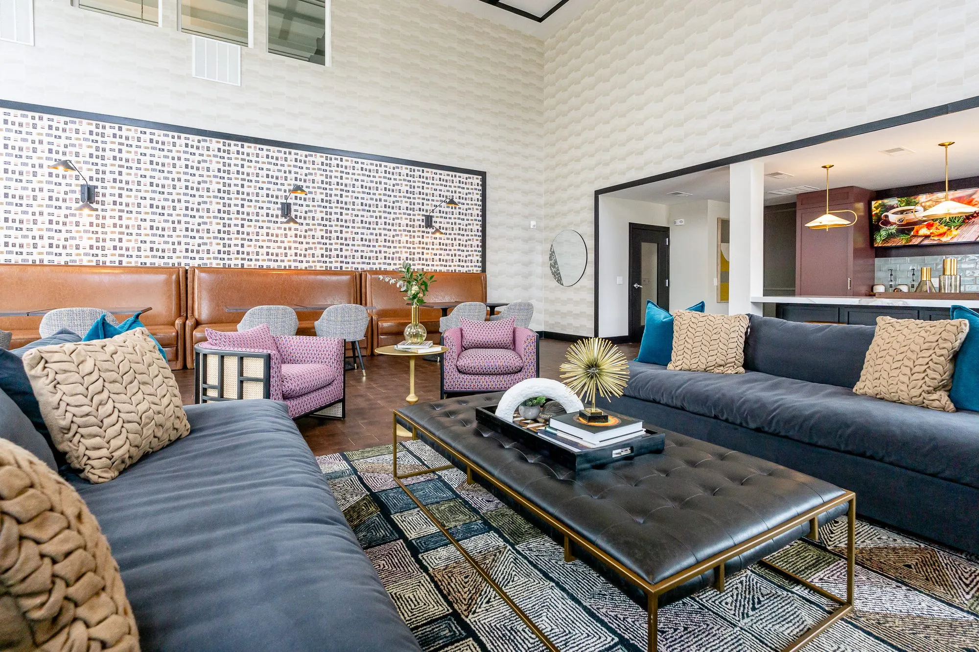 Multifamily amenity clubroom with navy sofas around a black tufted leather ottoman, leather booths and pink chairs beyond
