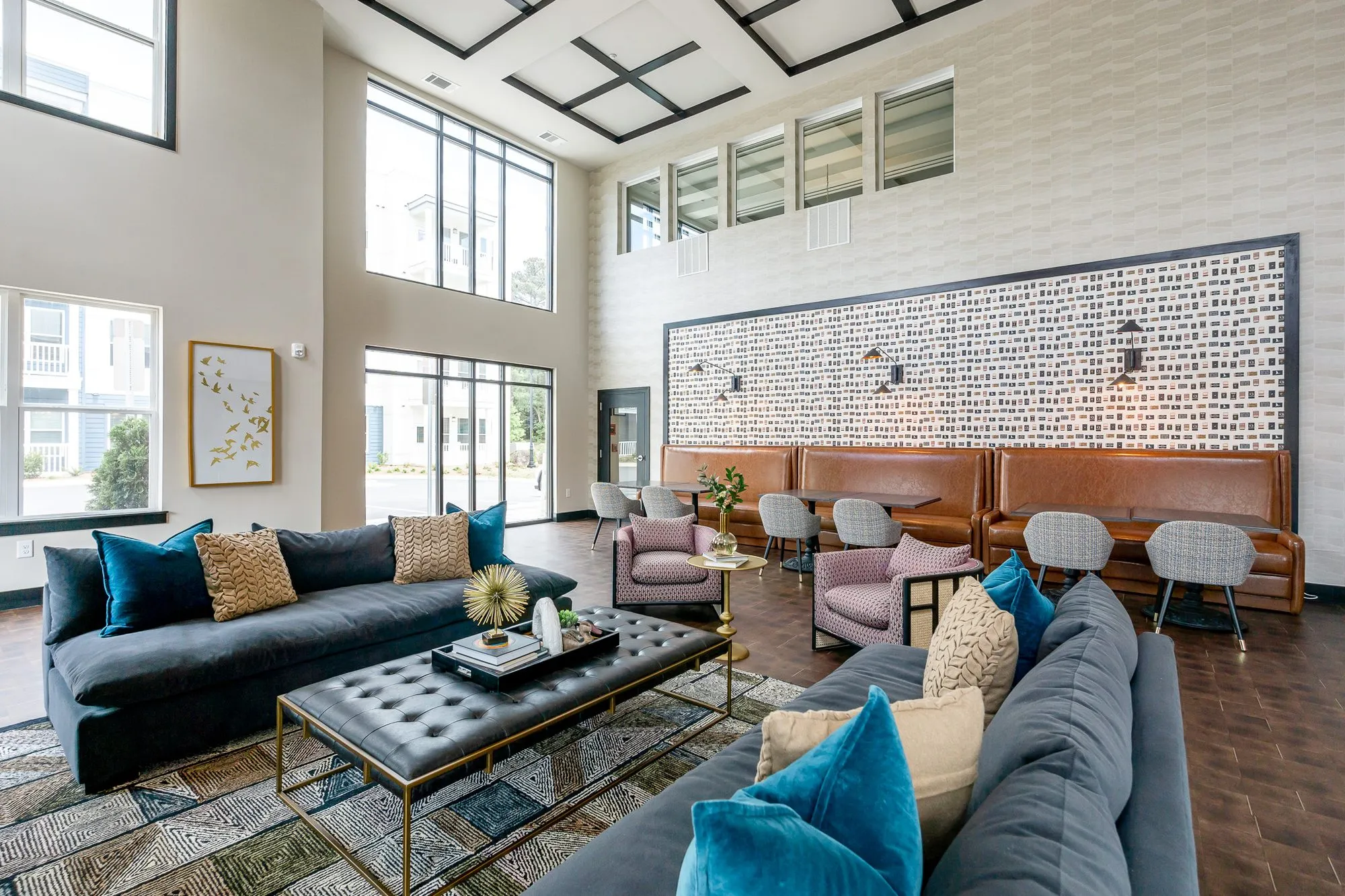 Multifamily amenity clubroom from the window side, tall windows at left and caramel leather booths along the patterned wall