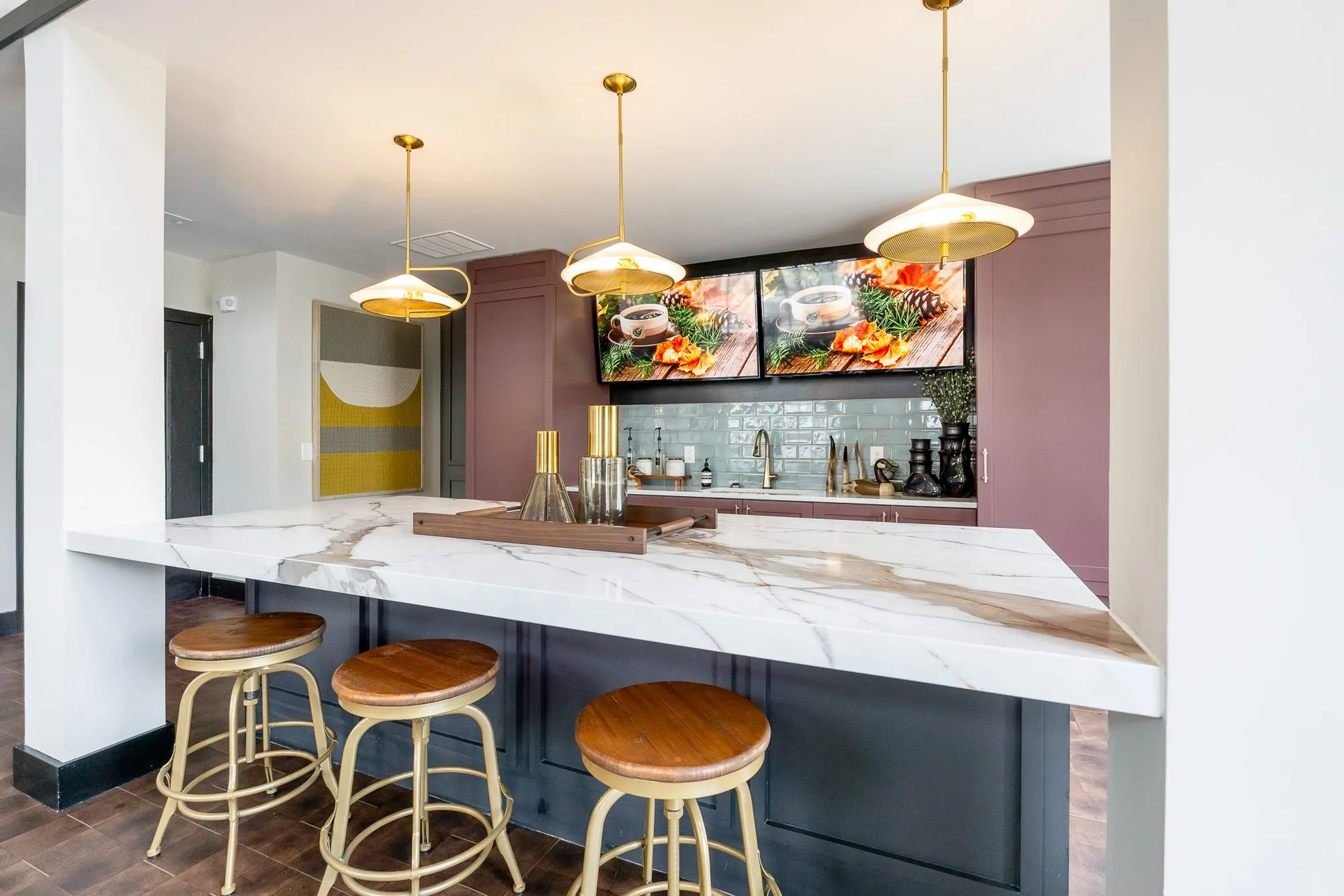 Multifamily amenity marble bar with three brass stools, a yellow and white artwork by the doorway at left