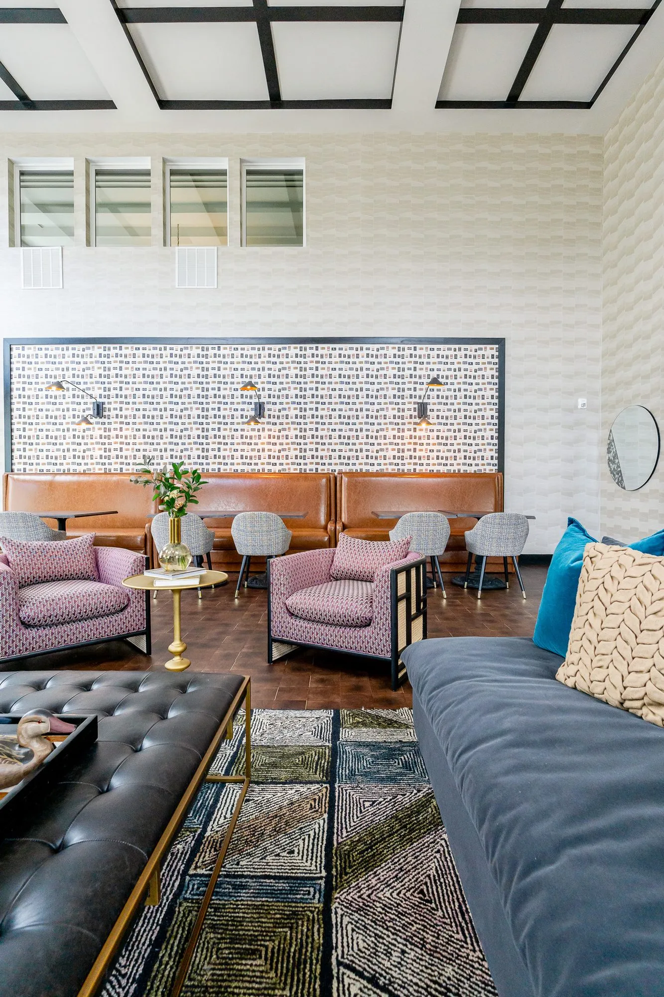 Multifamily amenity clubroom along a navy sofa and tufted leather ottoman toward pink armchairs and leather booths