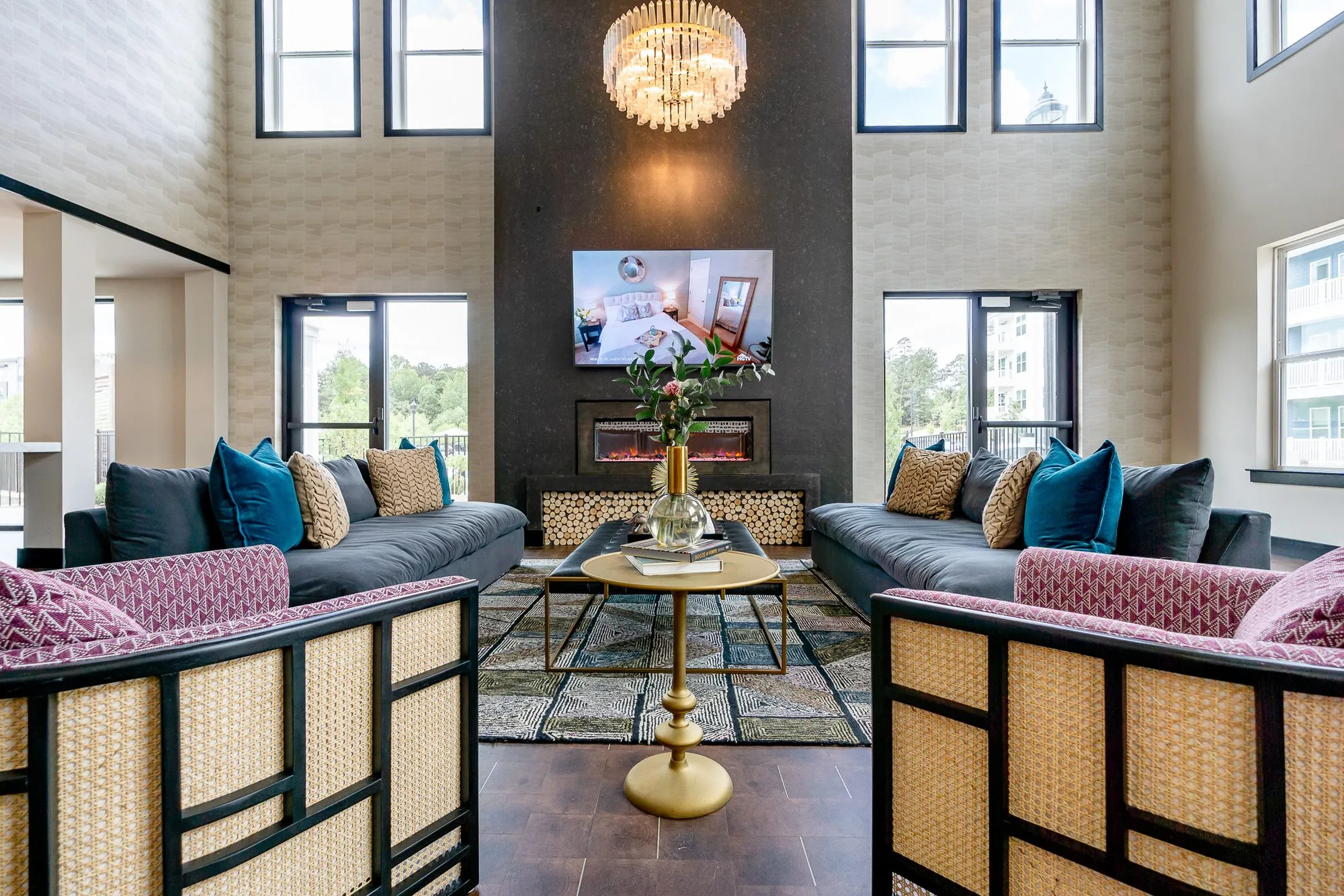 Multifamily amenity fireplace lounge with pink cane-framed armchairs flanking a brass table, a screen and crystal chandelier