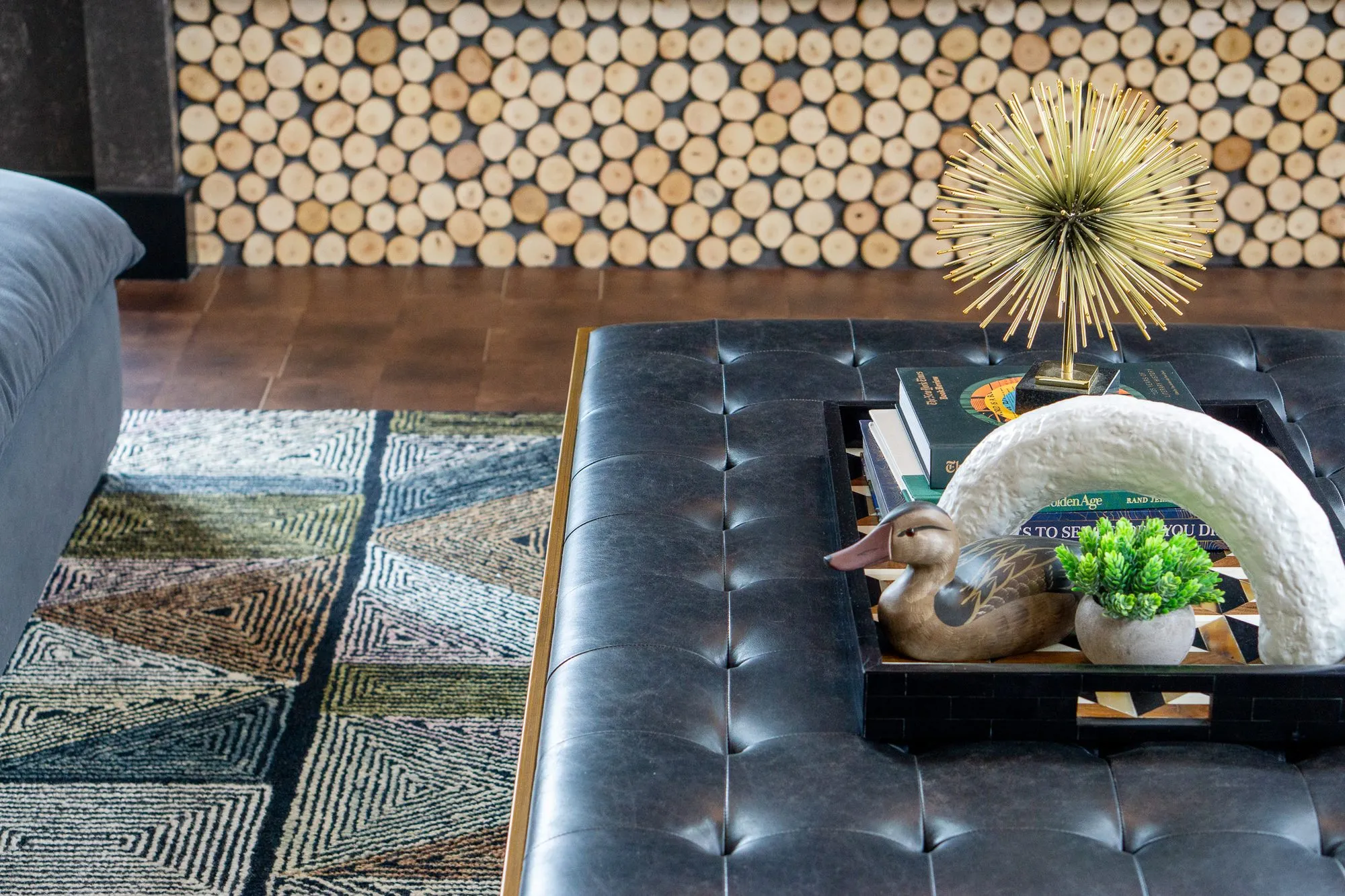 Multifamily amenity interior detail: tufted black leather ottoman with books, a duck decoy and starburst before log ends