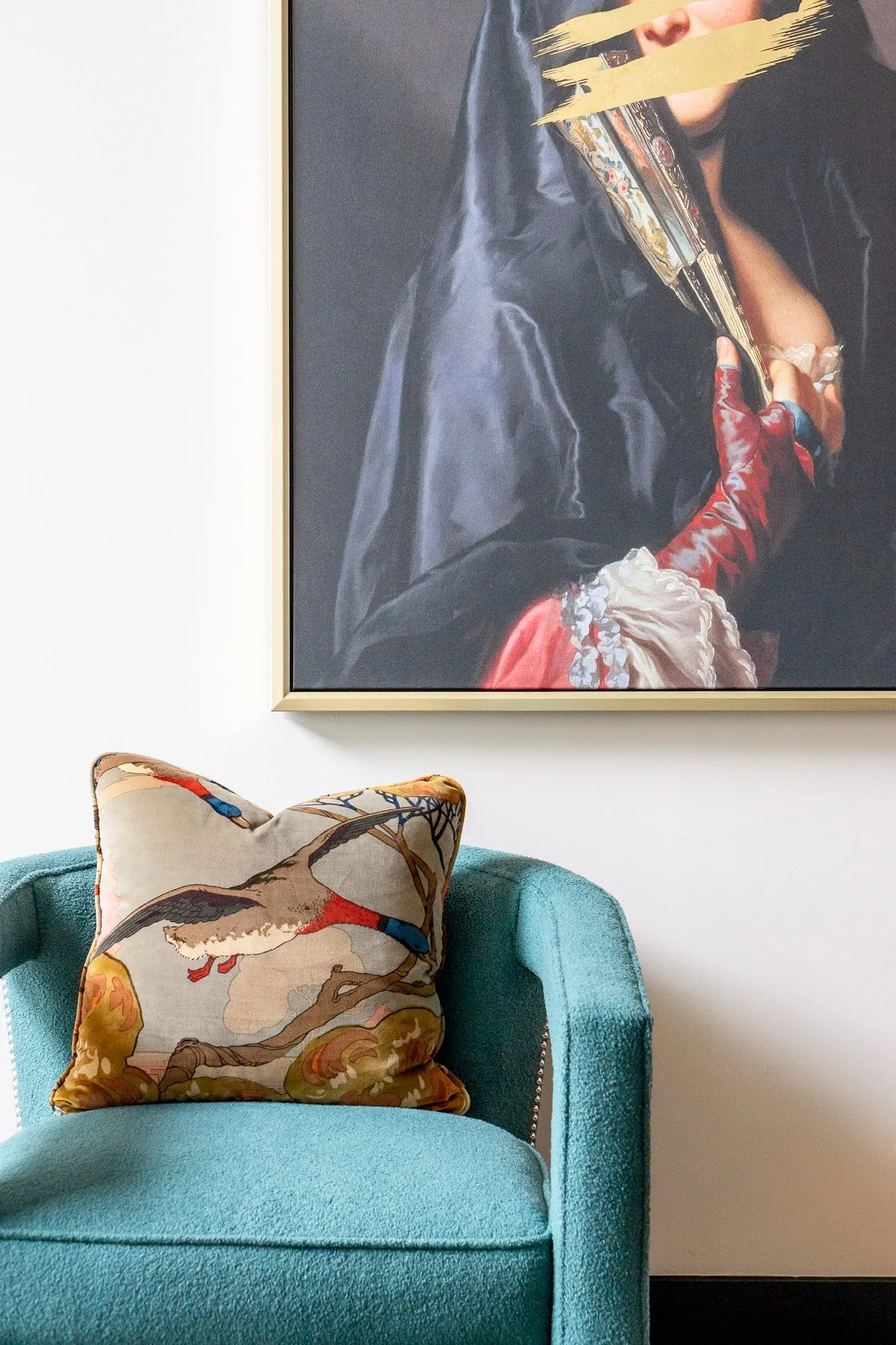 Multifamily amenity lobby lounge with a teal armchair and bird print pillow below the veiled portrait