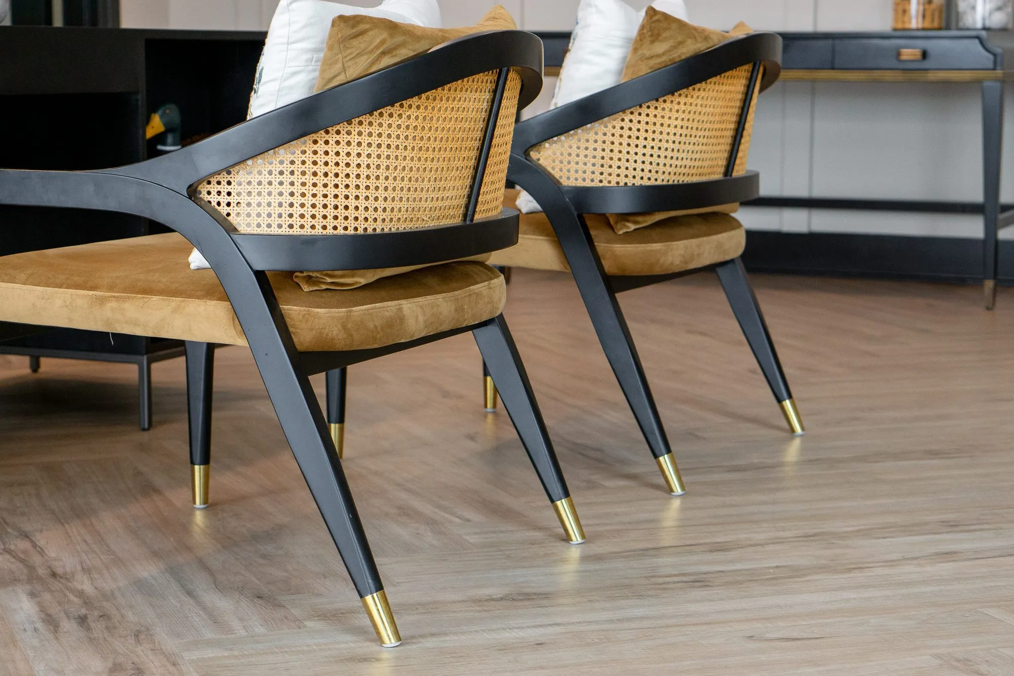 Multifamily amenity leasing area with two cane-back armchairs with black frames and gold-tipped legs on a herringbone floor