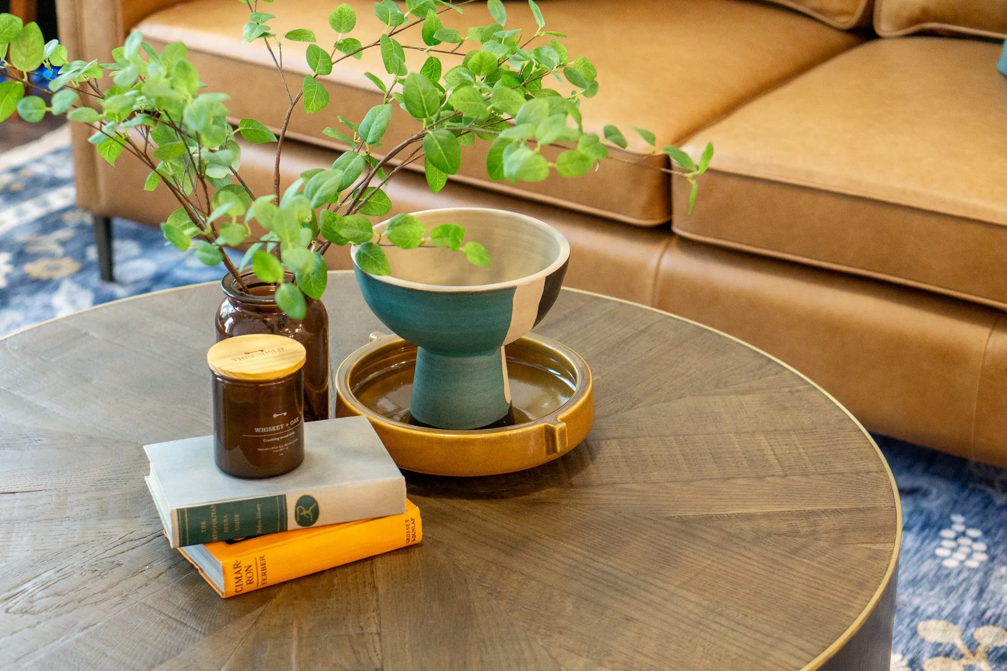Multifamily apartment model living room with a round wood coffee table, books and a teal bowl by a cognac leather sofa