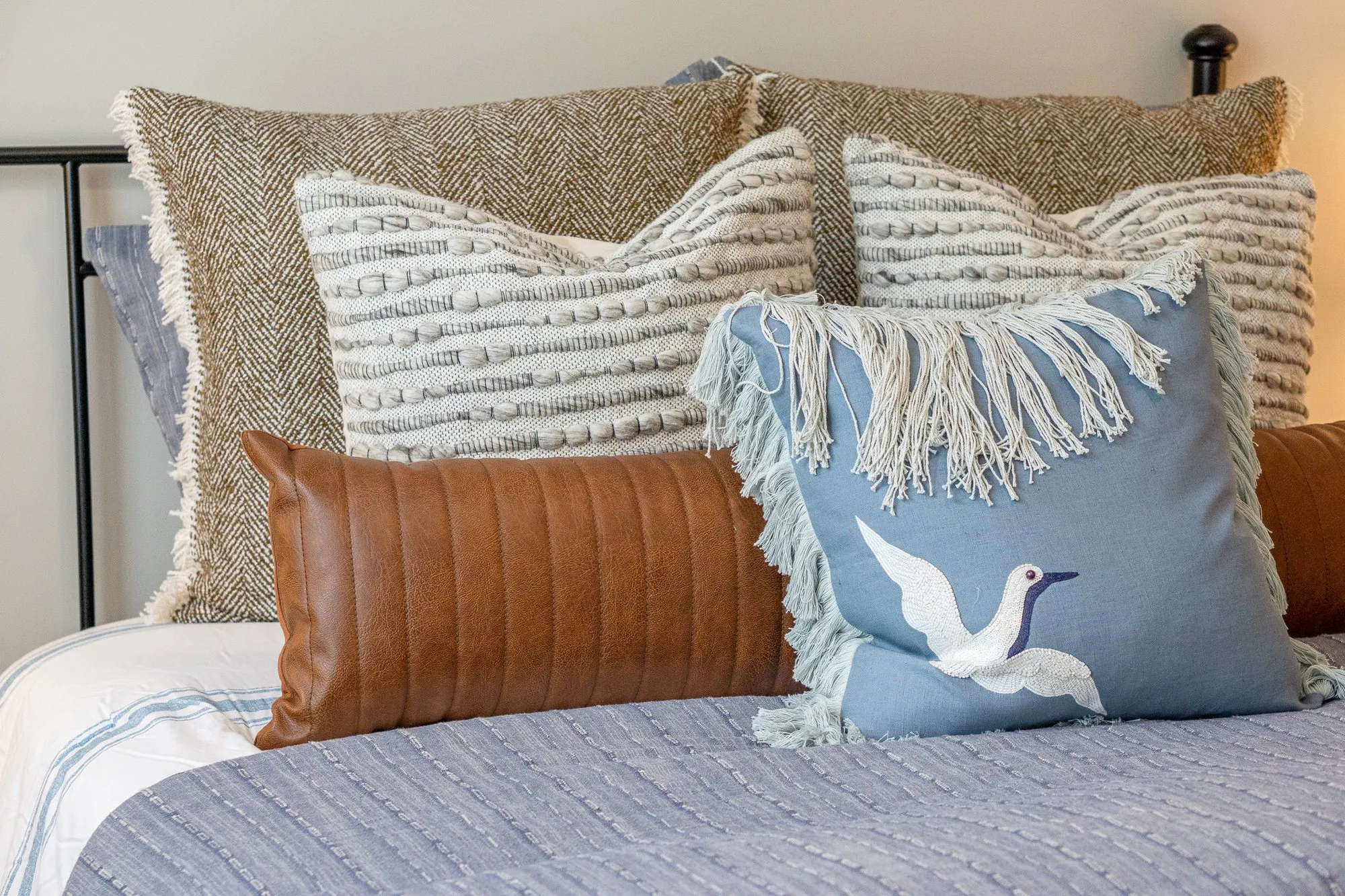 Multifamily interior detail: knit and fringed pillows, a leather lumbar pillow and a pillow embroidered with a flying bird