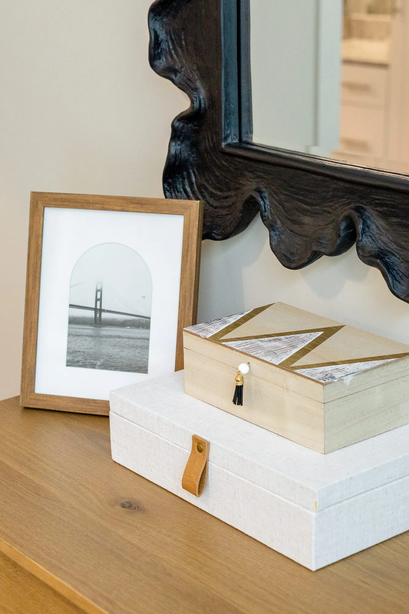 Multifamily interior detail: framed suspension bridge photograph and boxes on a wood dresser below a scalloped mirror