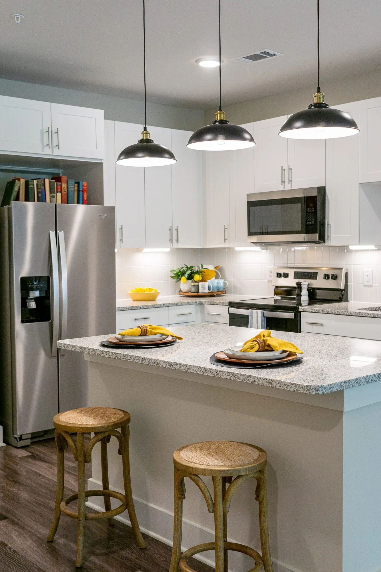 Multifamily apartment model kitchen with three black dome pendants above an island with wood stools