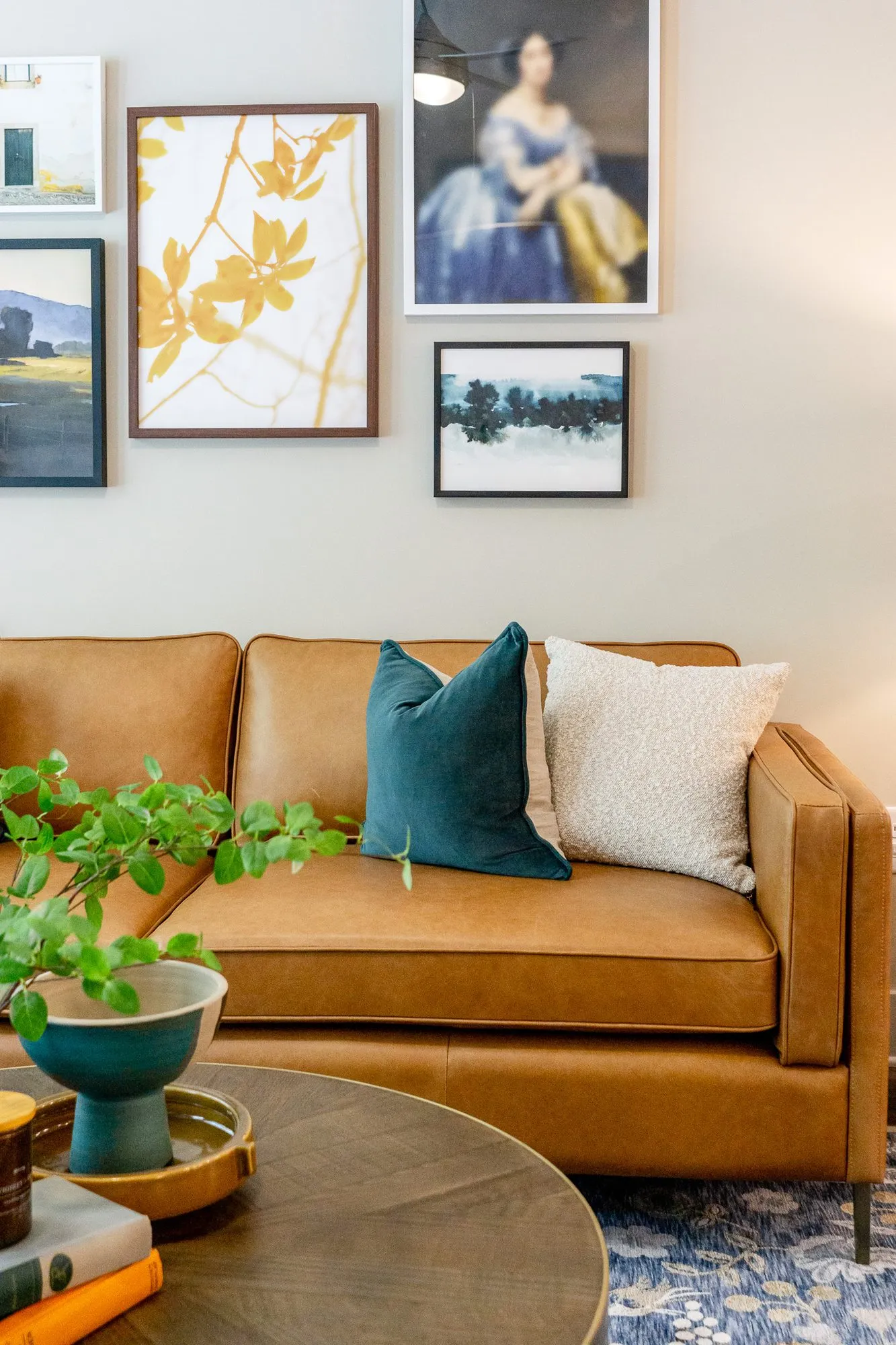 Multifamily apartment model living room with a cognac leather sofa, teal and cream pillows below a gallery of paintings