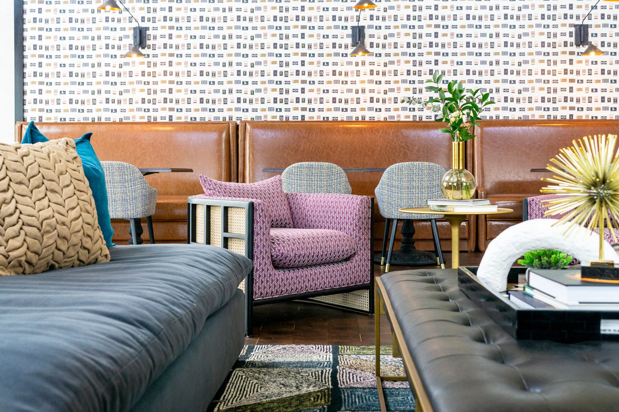 Multifamily amenity clubroom past a navy sofa and leather ottoman to a pink armchair and booths below matchbook wallpaper