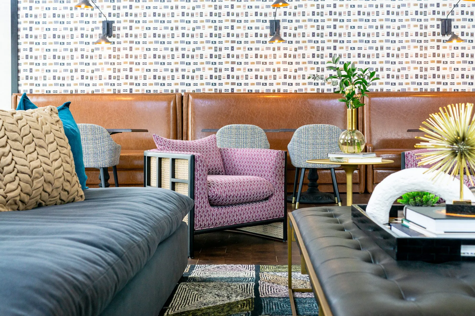 Multifamily amenity clubroom with a pink armchair between the navy sofa and leather ottoman, booths and sconces beyond