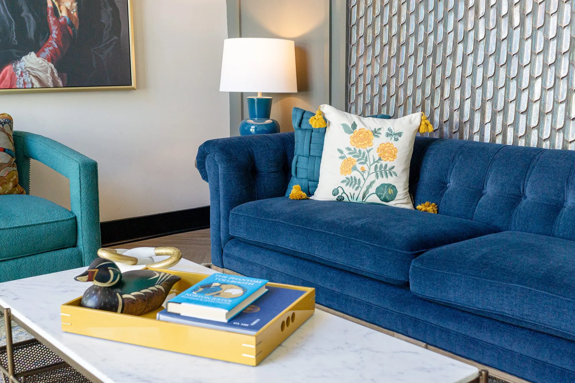 Multifamily amenity lobby lounge with a navy tufted sofa, floral and teal pillows and a duck decoy on the marble table