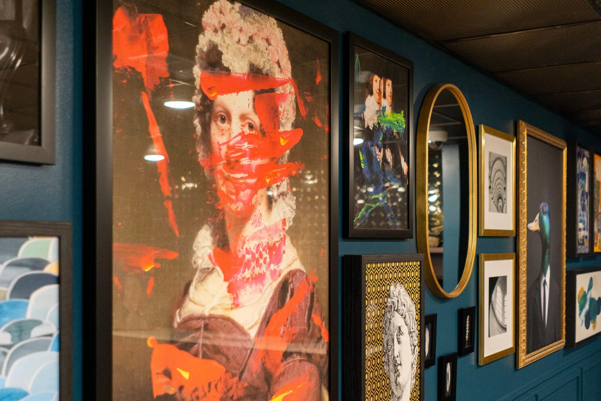 Multifamily amenity teal gallery wall with a red-streaked portrait, a bust print, an oval mirror and framed prints