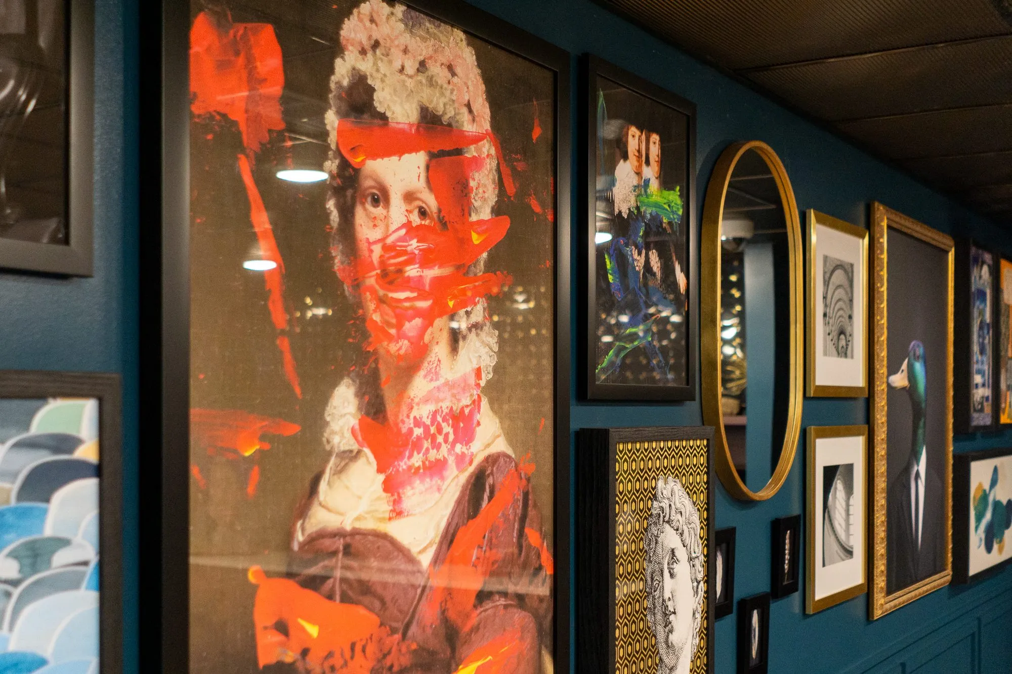 Multifamily amenity teal gallery wall from its end, the red-streaked portrait in front and frames receding beyond
