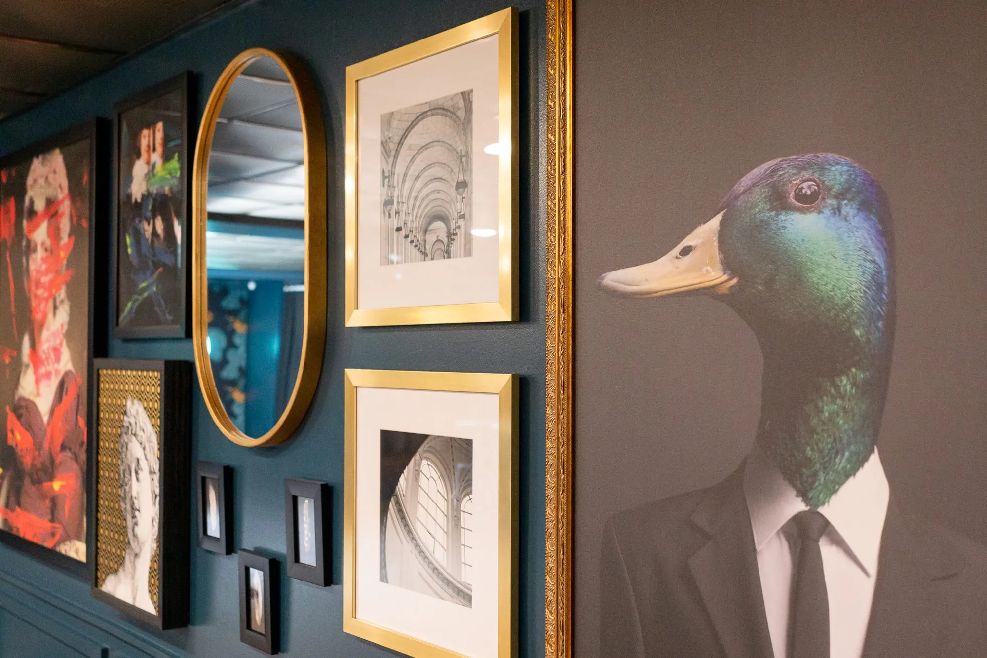 Multifamily amenity gallery wall with a duck-headed portrait in a suit beside gilt-framed architectural photographs