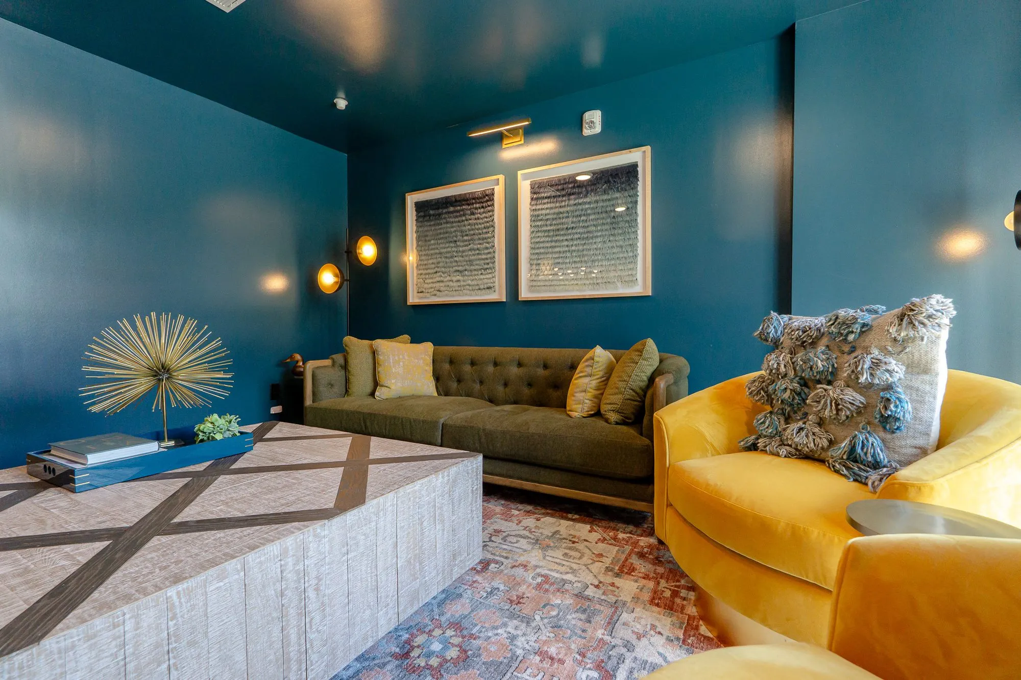 Multifamily interior detail: teal room with an olive tufted sofa, a yellow velvet swivel chair and a block coffee table