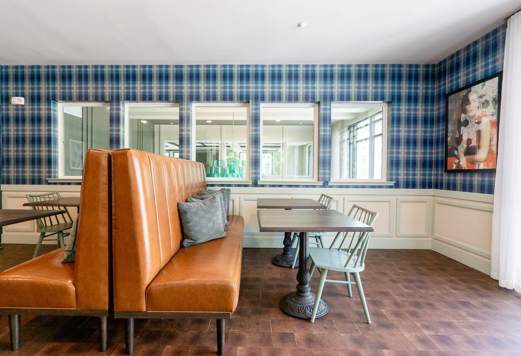 Multifamily amenity cafe with back-to-back cognac leather booths, wood tables and sage spindle chairs, blue plaid walls