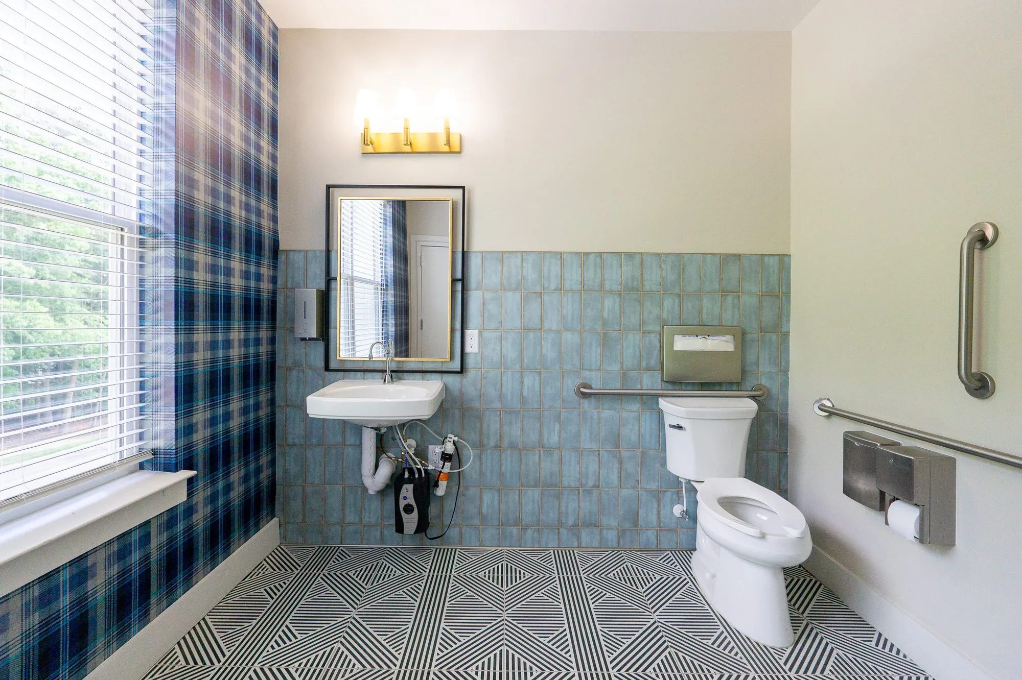 Multifamily amenity accessible restroom with blue glazed tile wainscot, plaid wallpaper and a black and white geometric floor