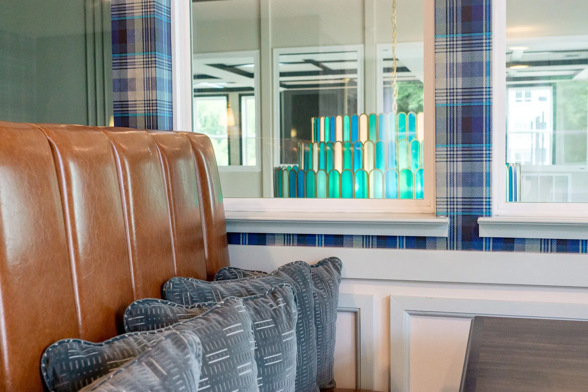 Multifamily amenity cafe with a cognac leather banquette below an interior window showing the glass chandelier
