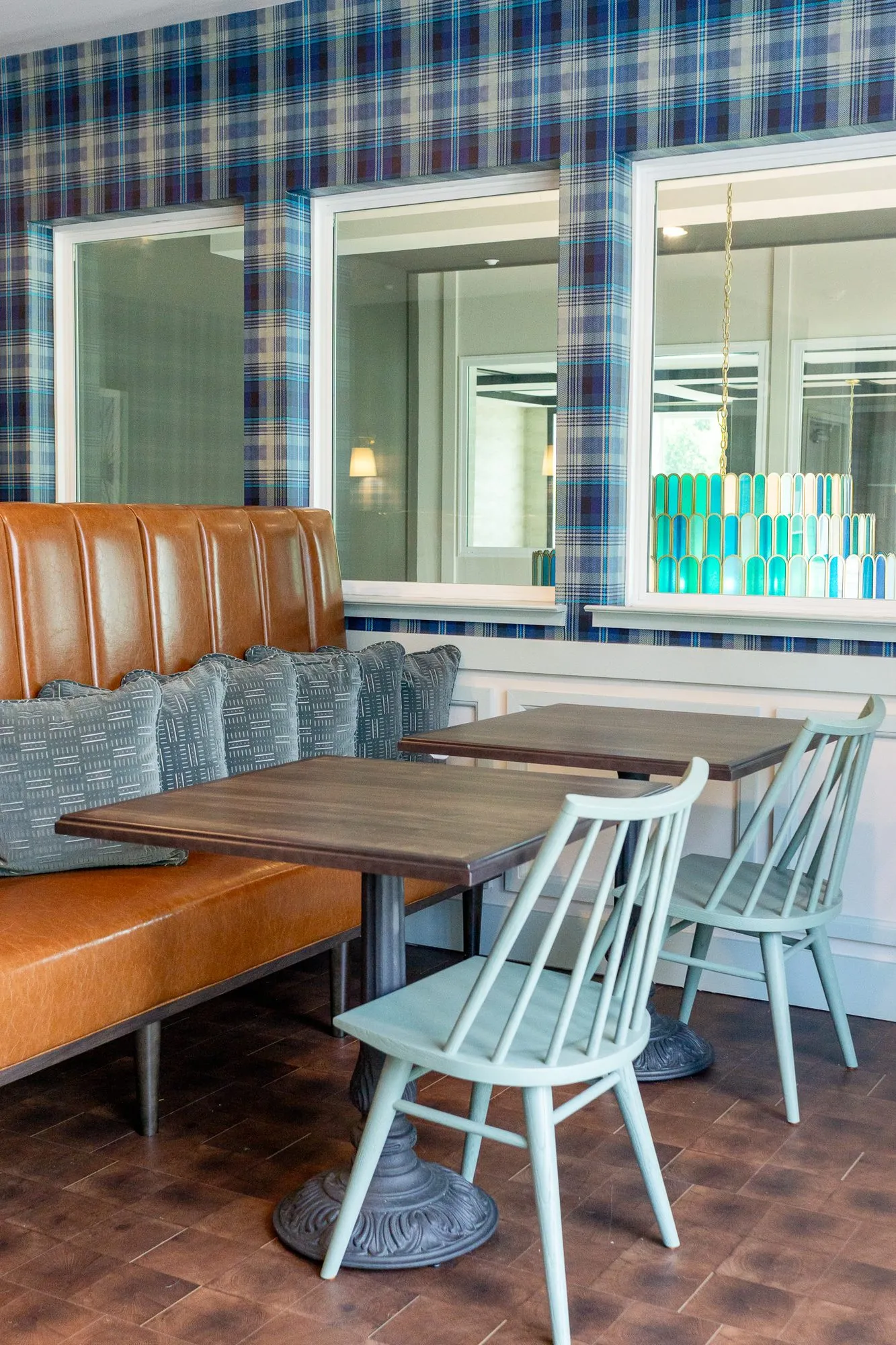 Multifamily amenity cafe with a wood table and sage spindle chairs beside the cognac banquette and plaid walls