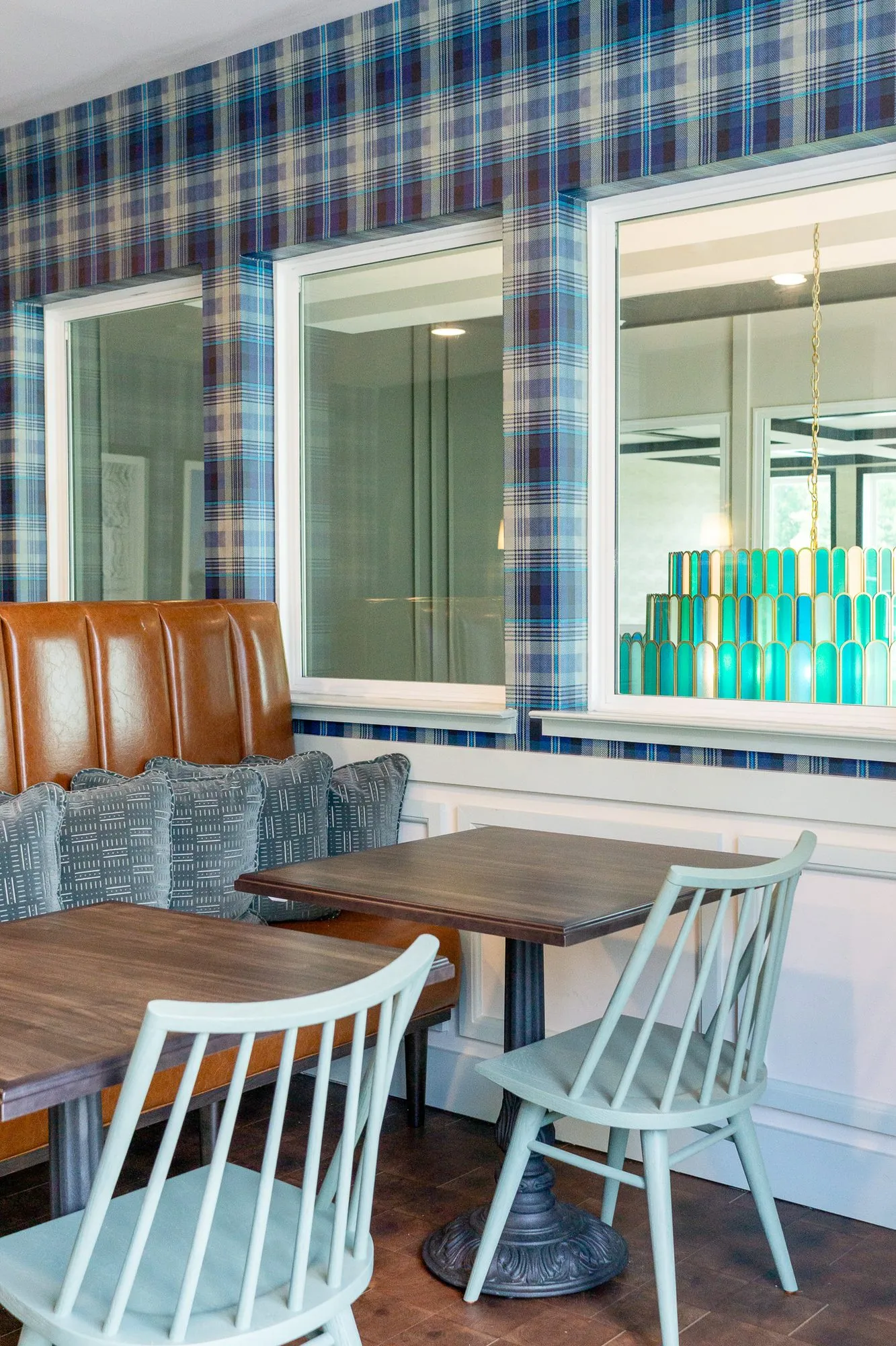 Multifamily amenity cafe with sage spindle chairs at wood tables under plaid wallpaper and interior windows