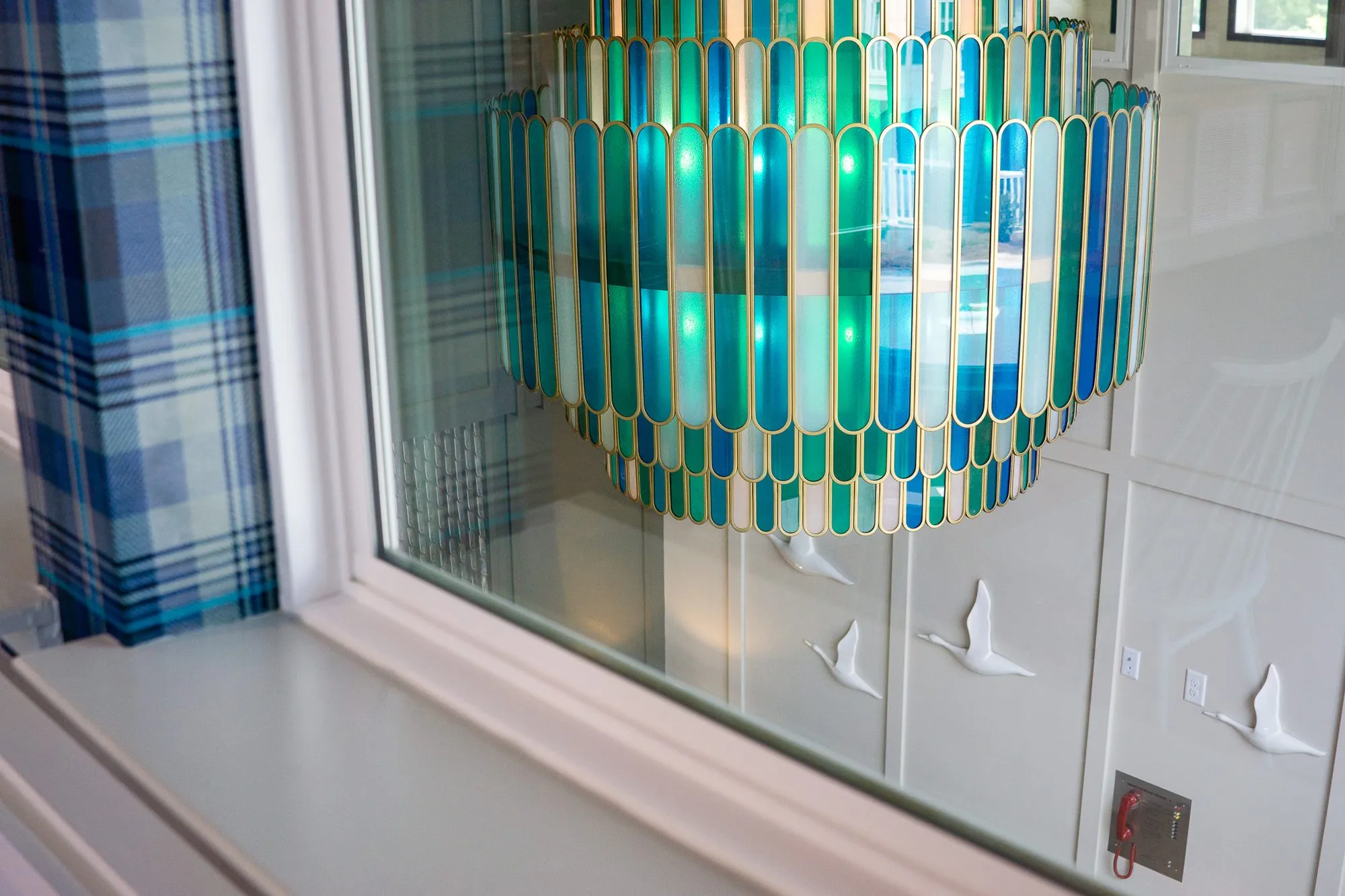 Multifamily amenity cafe interior window framed in plaid wallpaper, the glass chandelier seen through it