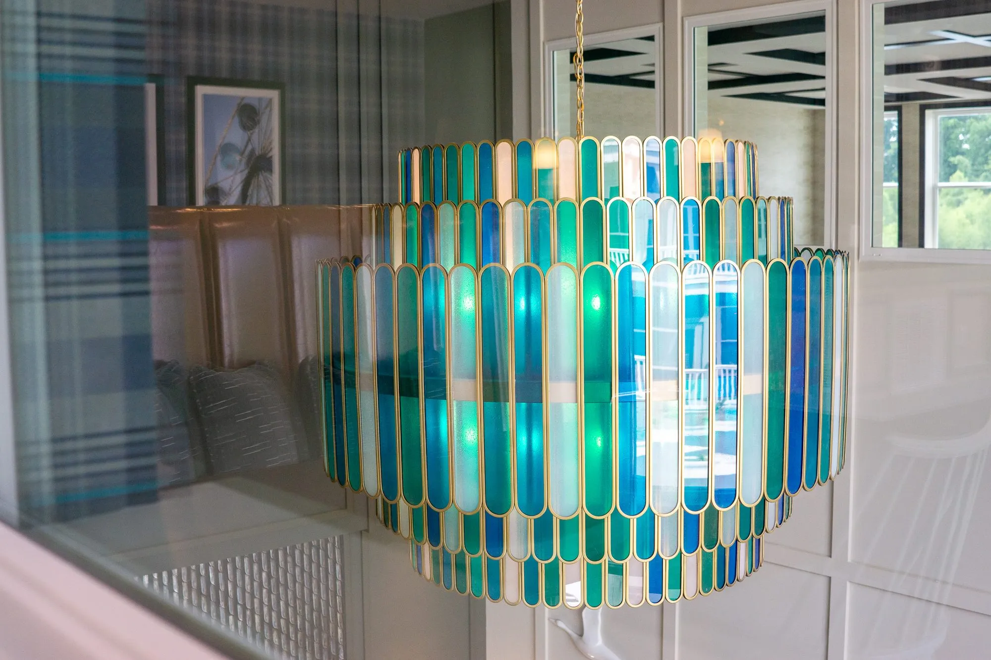 Multifamily amenity cafe interior window with the tiered blue and green glass chandelier beyond, the plaid wall reflected