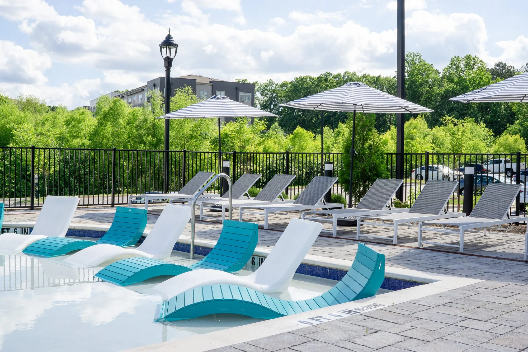 Multifamily community pool with teal and white in-water loungers on the sun shelf, grey chaises and striped umbrellas